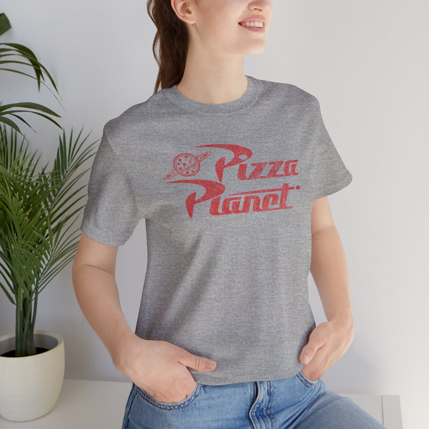 Woman wearing heather gray t-shirt with distressed red Pizza Planet logo inspired by the Toy Story movies.