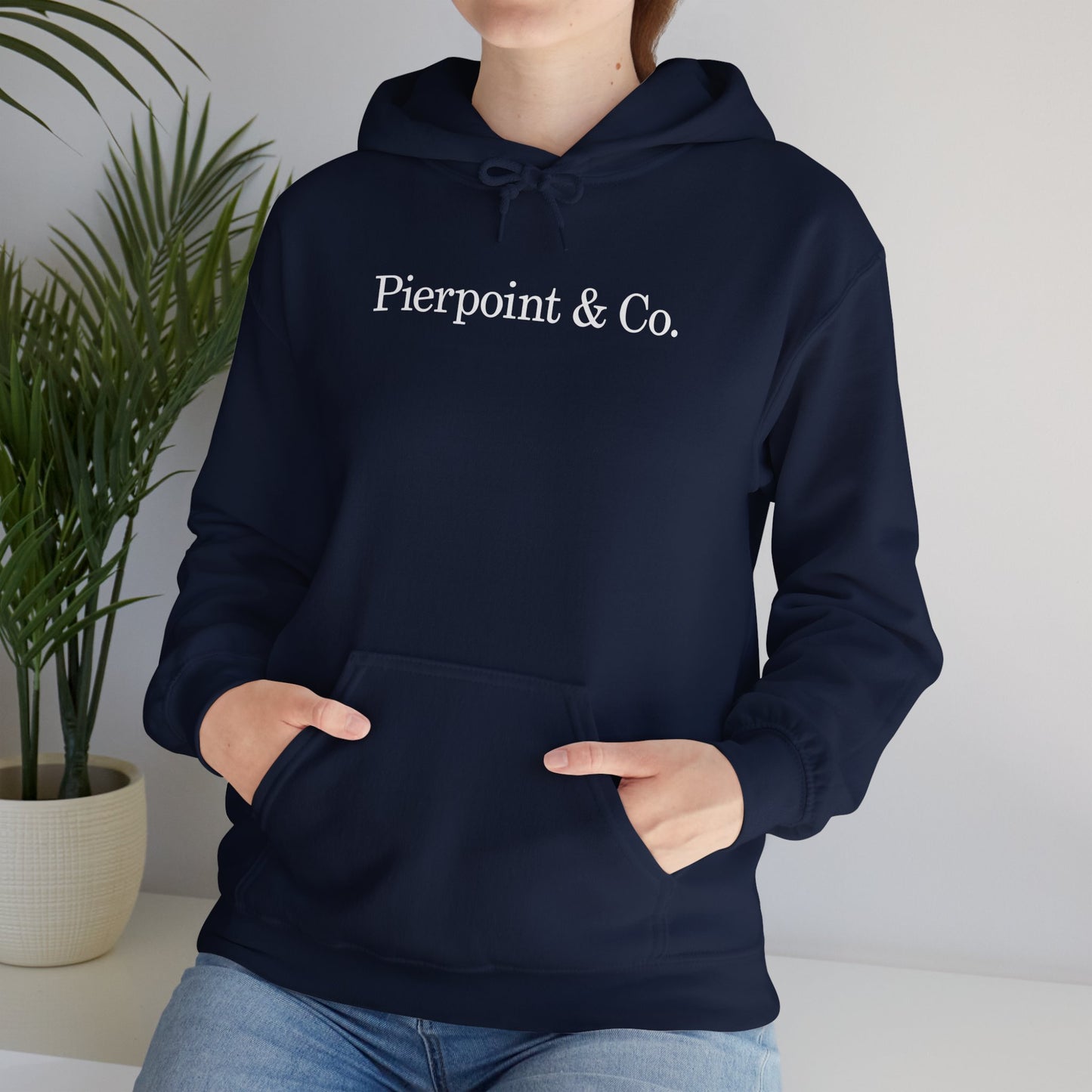 Female model wearing a navy blue soft Unisex Hoodie Heavy Blend Hooded Sweatshirt featuring the Pierpoint & Co logo worn by the character Eric Tao in the TV show Industry.
