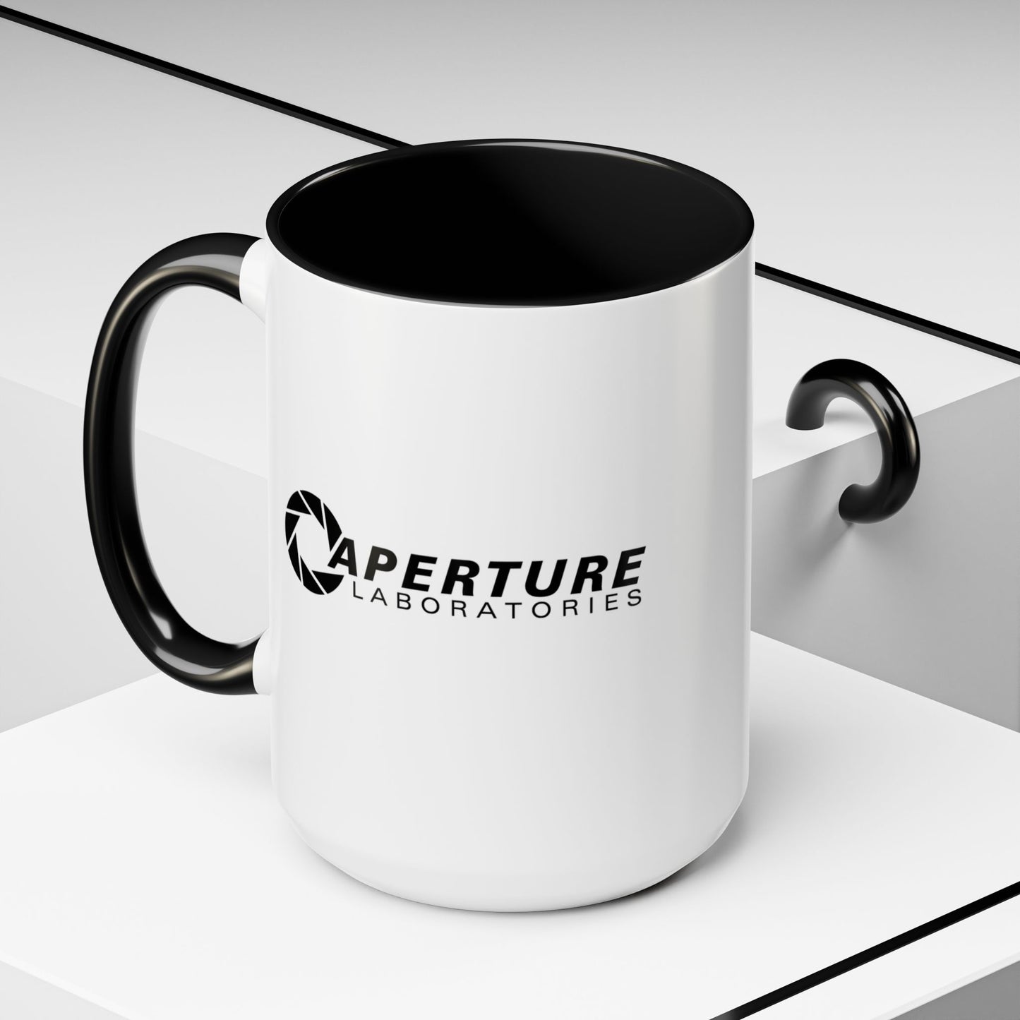 Front angled view of a 15 oz white Ceramic Accent Mug with the black Aperture Laboratories logo from the video game Portal on both sides. Handle and interior are colored black.