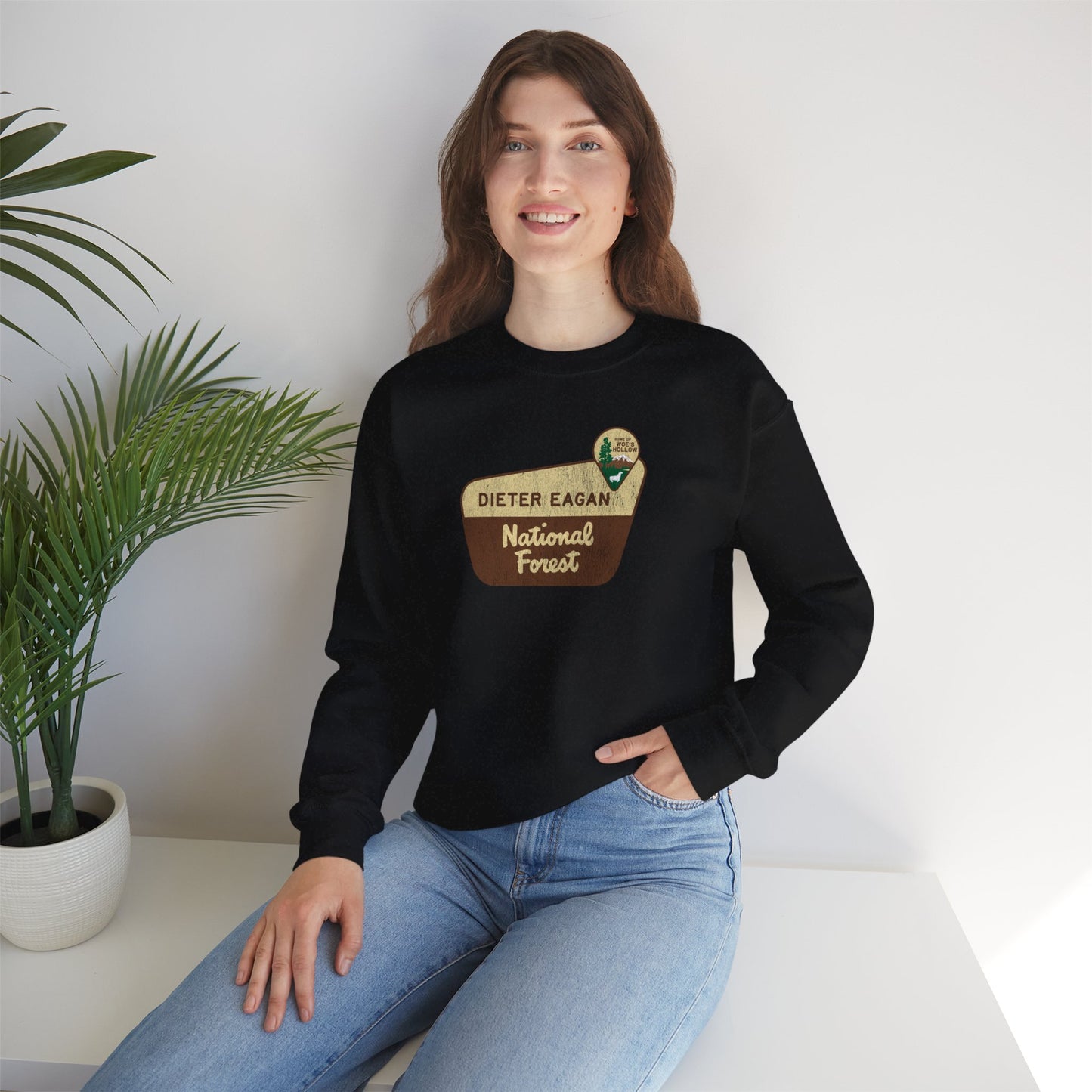 Female model wearing a black Soft Unisex Gildan 18000 sweatshirt featuring a logo graphic of the Dieter Eagan National Forest sign designed by ScriptedBrand, inspired by the TV show Severance in a vintage distressed style.