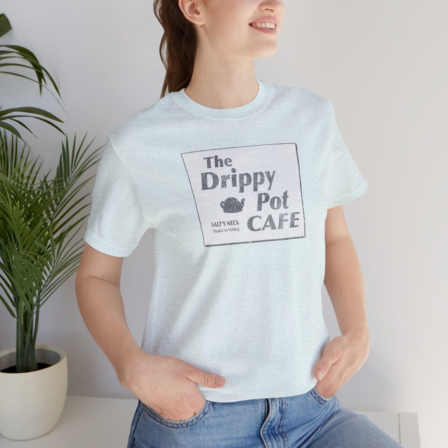Female wearing Bella+Canvas heather ice blue short-sleeve t-shirt featuring vintage Drippy Pot Café logo from Severance TV show, unisex fit
