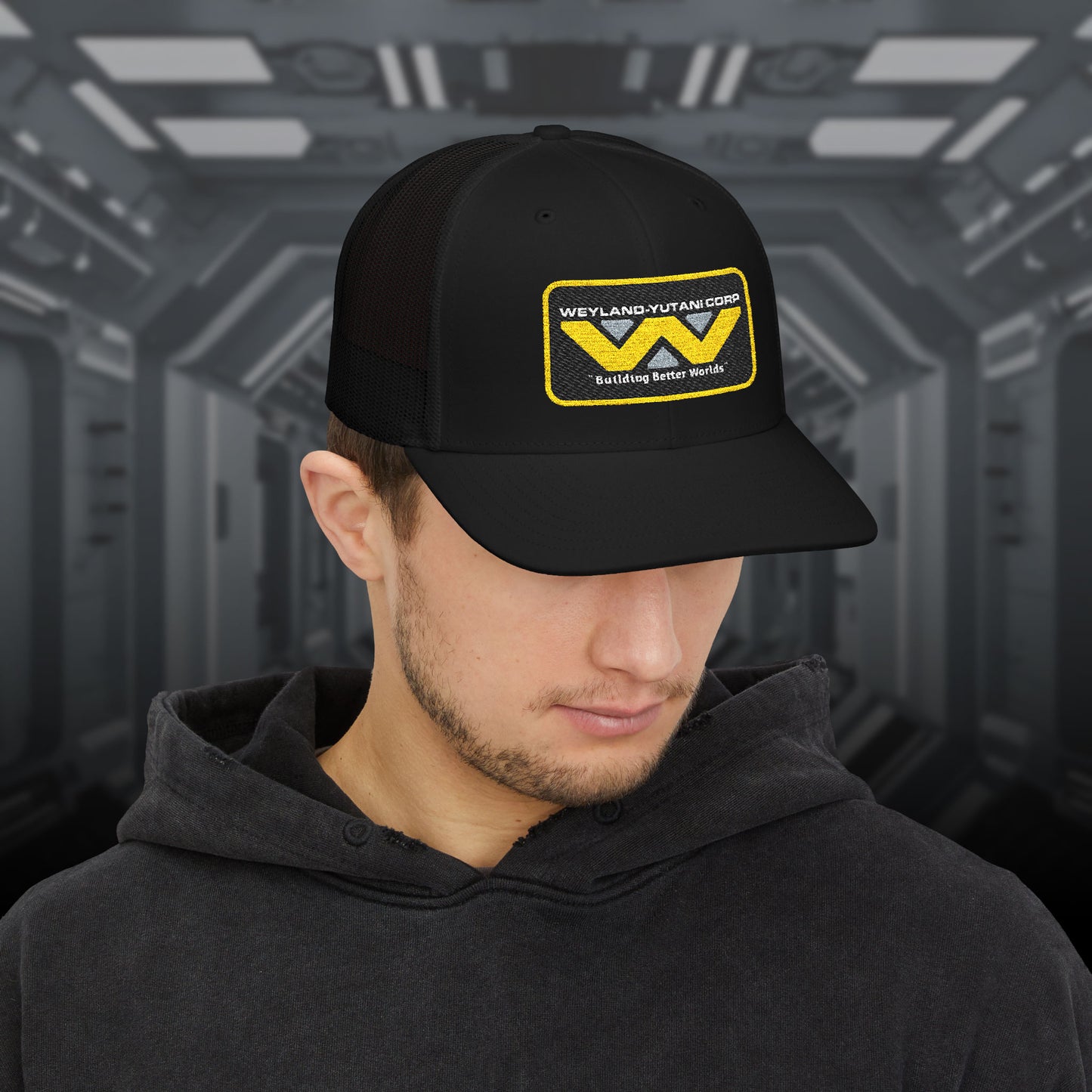 Man wearing black Embroidered Snapback Trucker Cap with logo of Weyland-Yutani from the Alien movie franchise.