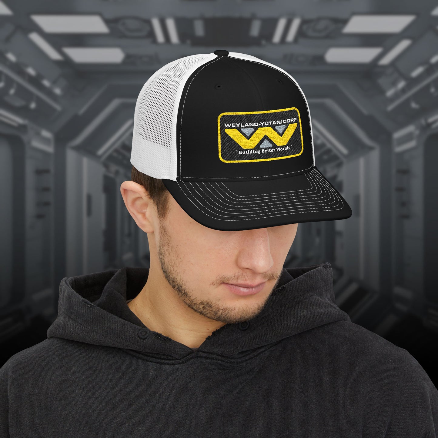 Man wearing black-white Embroidered Snapback Trucker Cap with logo of Weyland-Yutani from the Alien movie franchise.