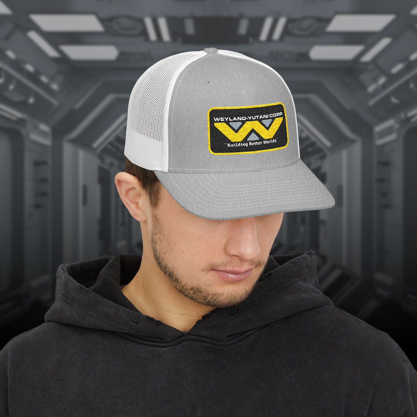 Man wearing gray-white Embroidered Snapback Trucker Cap with logo of Weyland-Yutani from the Alien movie franchise.