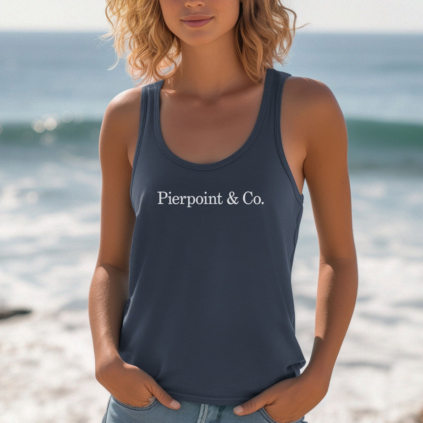 Female model wearing a indigo blue colored Women's Racerback Tank Top Shirt featuring the Pierpoint & Co logo from the HBO TV show Industry, sold by ScriptedBrand.