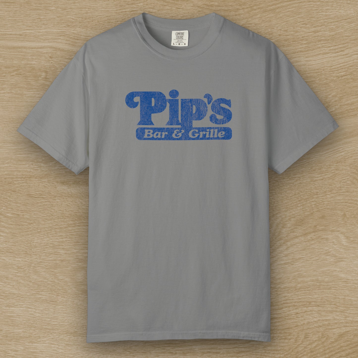 Vintage-style Pip’s Bar & Grill t-shirt from Severance on Comfort Colors 1717 in the color granite, blue distressed logo.