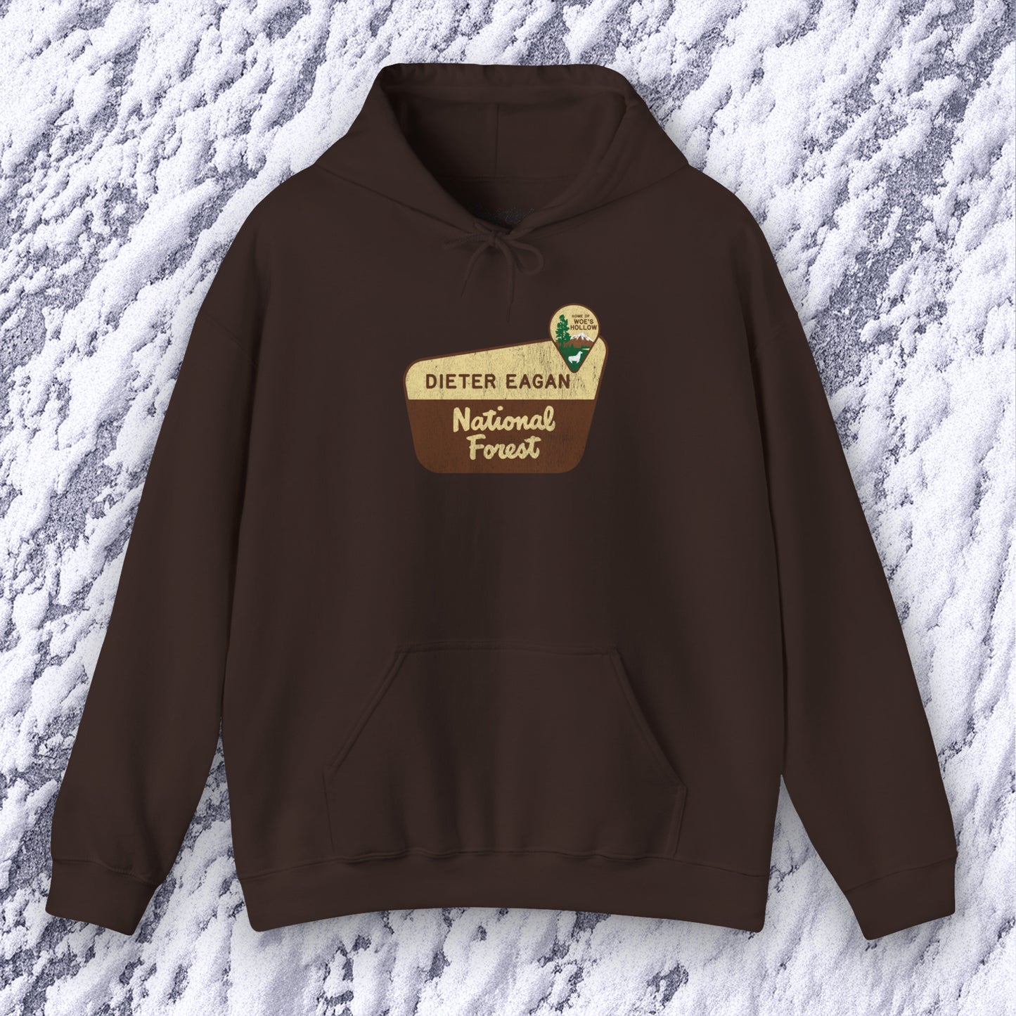 Mockup of a dark chocolate colored Soft Unisex Hoodie Heavy Blend Hooded Sweatshirt featuring the logo graphic of the Dieter Eagan National Forest inspired by the TV show Severance in a vintage distressed ink-stamped worn-in style.