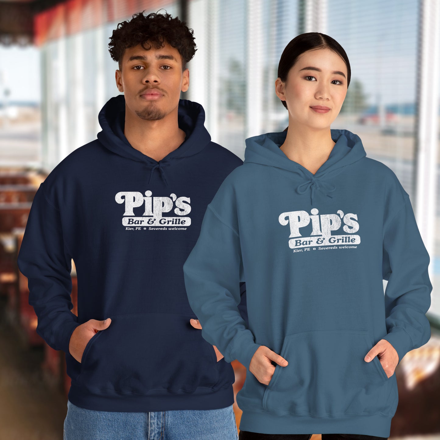 2 models in a diner wearing Soft Unisex Hoodie Heavy Blend Hooded Sweatshirts featuring the Pips Bar & Grill logo, with the added text "Severeds Welcome" inspired by the TV show Severance in a vintage distressed style, sold by ScriptedBrand.