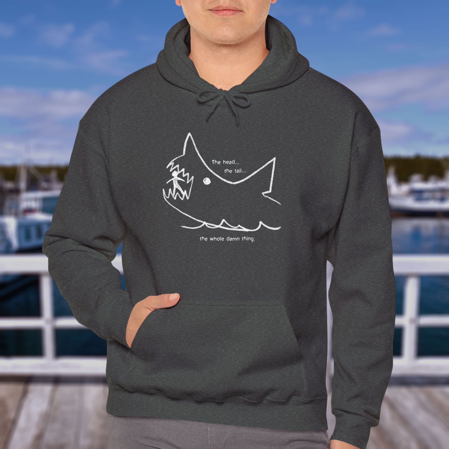Male model wearing a Dark Heather Gray colored Soft Unisex Hoodie Heavy Blend Hooded Sweatshirt with the chalkboard drawing of a shark eating a person, drawn by Quint in the movie Jaws.