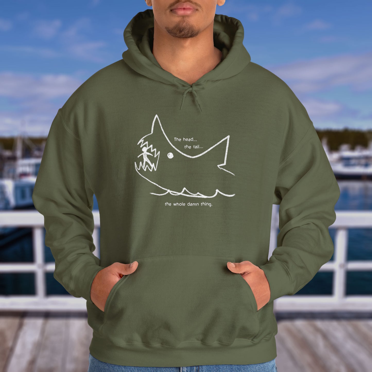 Male model wearing a Military Green colored Soft Unisex Hoodie Heavy Blend Hooded Sweatshirt with the chalkboard drawing of a shark eating a person, drawn by Quint in the movie Jaws.