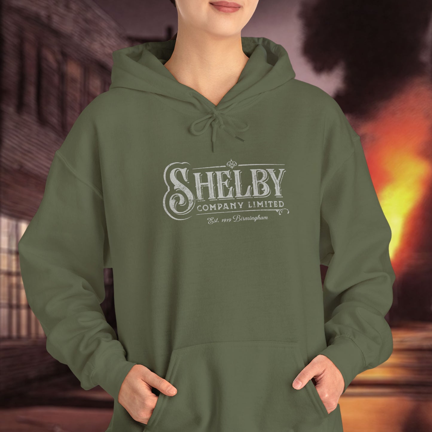 Female model wearing a military green colored Soft Unisex Hoodie Heavy Blend Hooded Sweatshirt featuring the fictional logo Shelby Company Limited from the TV series Peaky Blinders in a vintage distressed style.