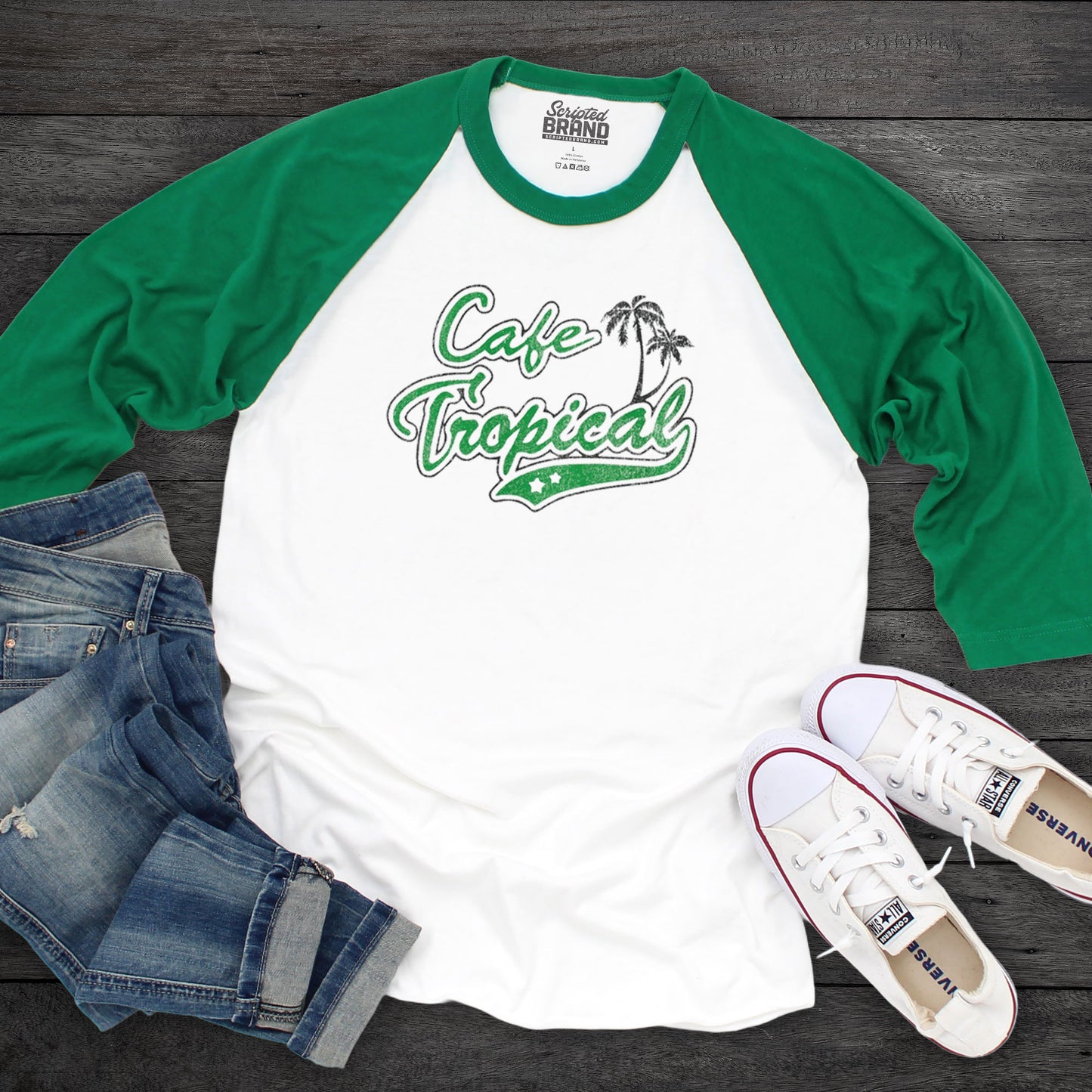 Flatlay overhead view of a white and Green colored soft raglan 3/4 sleeve Tultex 245 baseball shirt featuring the fictional Cafe Tropical logo that David wore in the TV Show Schitts Creek in a vintage distressed style, sold by ScriptedBrand.
