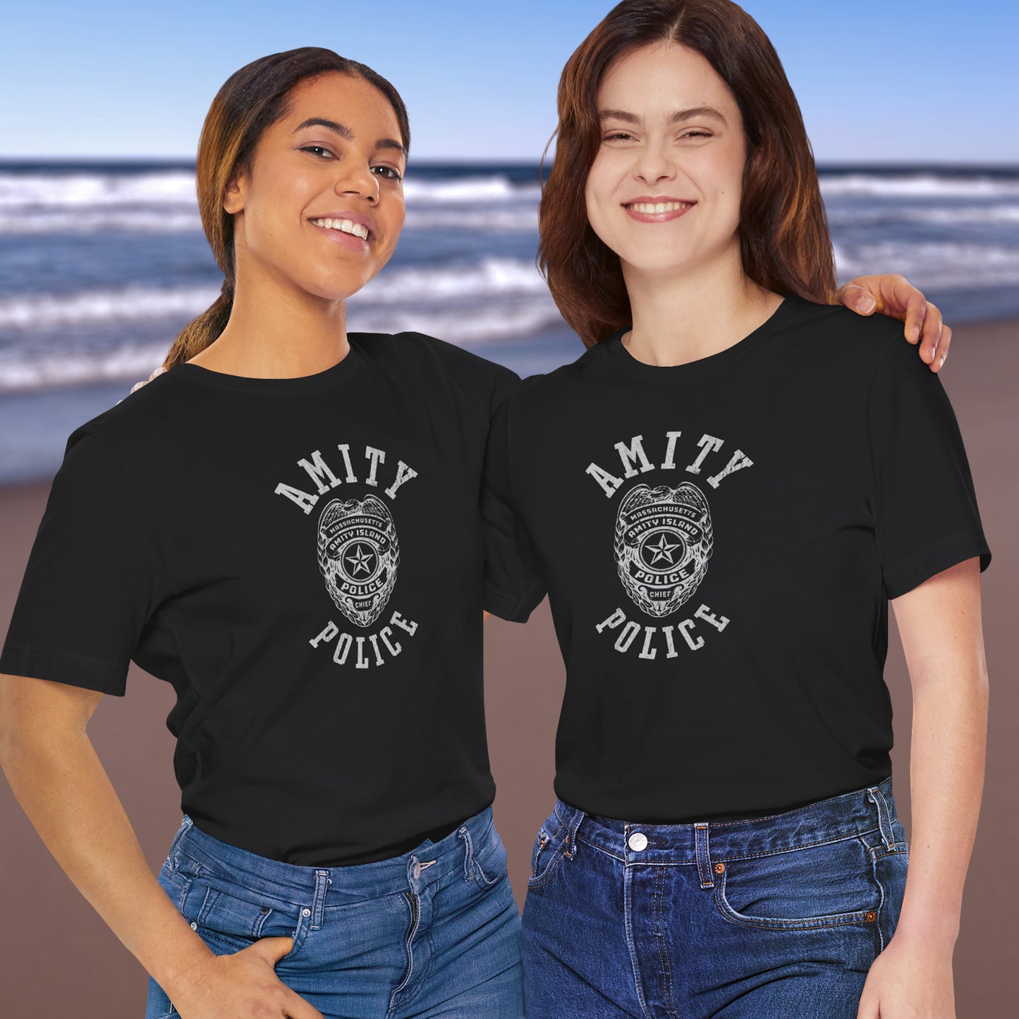 2 female models wearing black colored Soft unisex Bella+Canvas 3001 short-sleeve t-shirts featuring an Amity Island Police logo graphic, designed by ScriptedBrand, and inspired by the movie Jaws in a vintage distressed style.