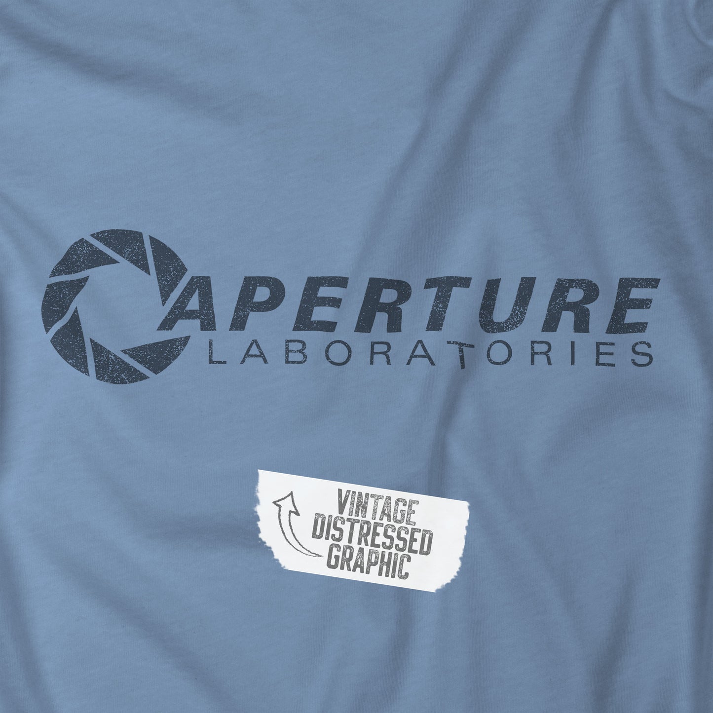 Closeup view of a steel blue colored soft Bella+Canvas t-shirt with the Aperture Laboratories logo from the video game Portal and Portal 2 in a vintage ink-stamped distressed style.