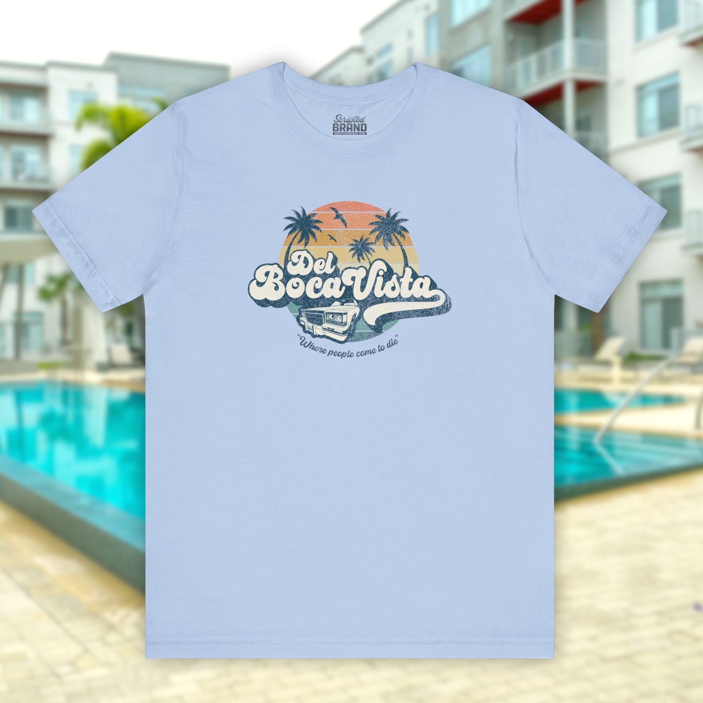 Front view of a baby blue Soft Bella+Canvas 3001 short-sleeve t-shirt featuring a Del Boca Vista logo graphic (uniquely designed by ScriptedBrand), including the phrase Where People Come To Die, inspired by the TV show Seinfeld, in a vintage distressed style.