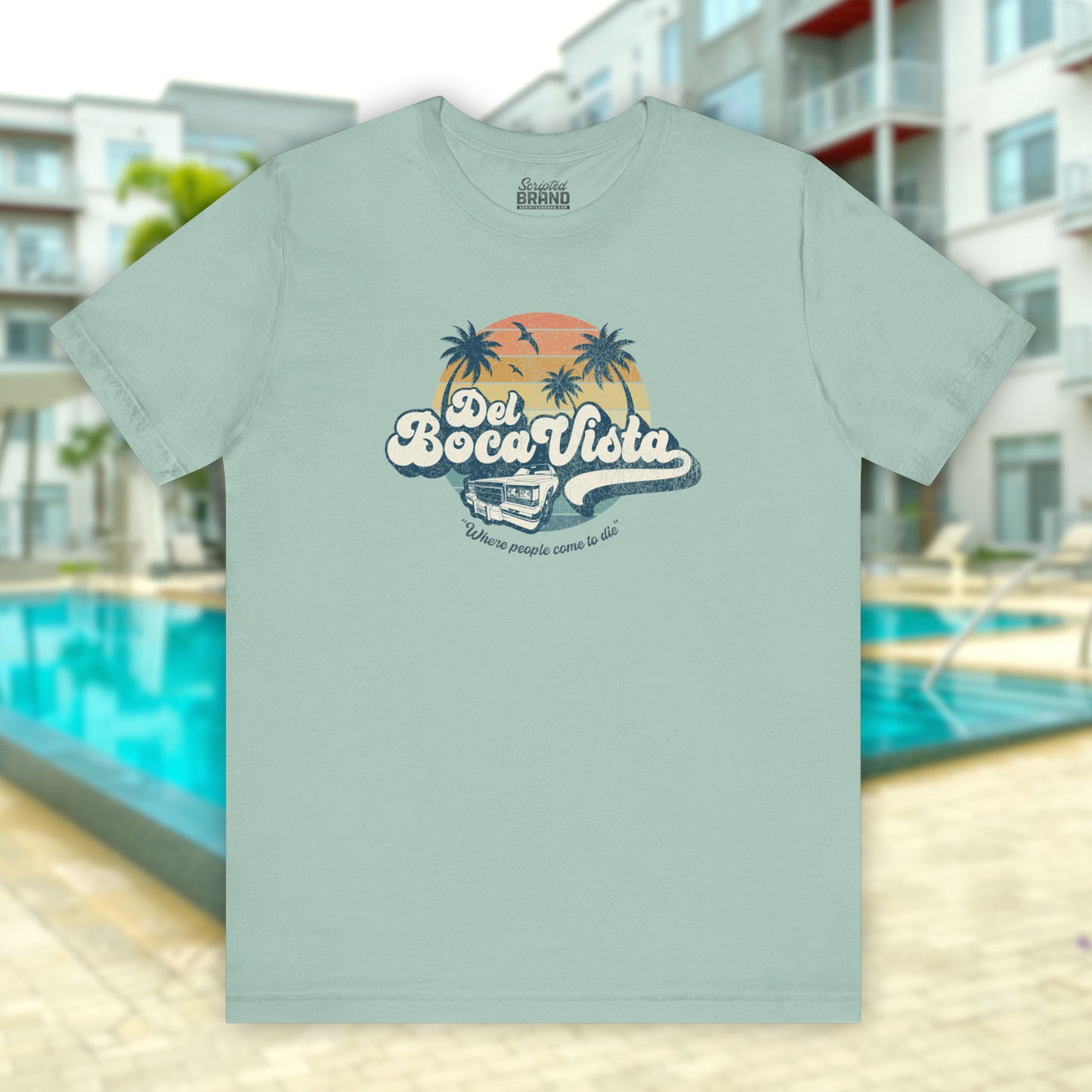 Front view of a dusty blue Soft Bella+Canvas 3001 short-sleeve t-shirt featuring a Del Boca Vista logo graphic (uniquely designed by ScriptedBrand), including the phrase Where People Come To Die, inspired by the TV show Seinfeld, in a vintage distressed style.