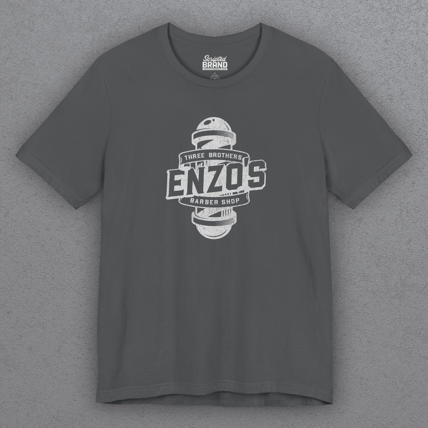 Front view of an asphalt gray t-shirt with the Enzo's Barber Shop logo graphic inspired by the TV show Seinfeld in a vintage distressed style.