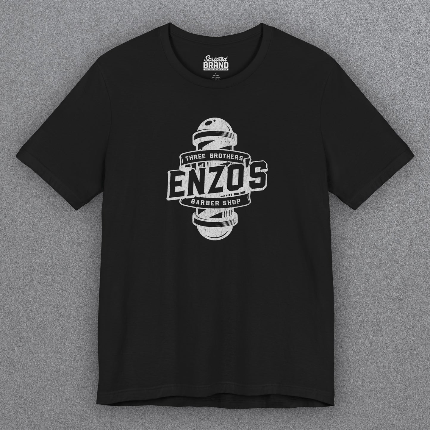 Front view of a black t-shirt with the Enzo's Barber Shop logo graphic inspired by the TV show Seinfeld in a vintage distressed style.