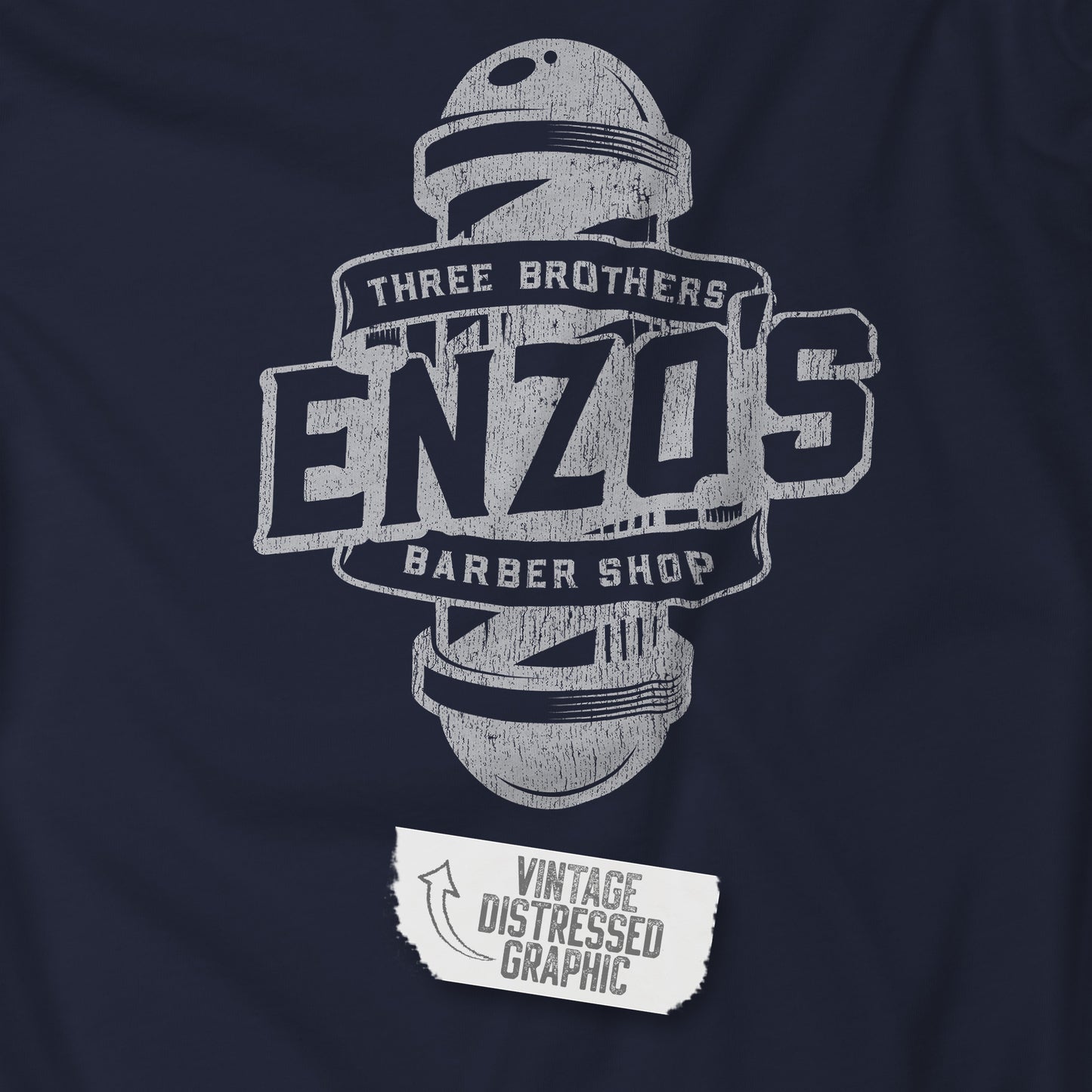 Closeup view of a navy blue soft unisex Bella+Canvas 3001 short-sleeve t-shirt featuring a unique Enzo's Barber Shop logo graphic, designed by ScriptedBrand in a vintage distressed style, and inspired by the TV show Seinfeld.