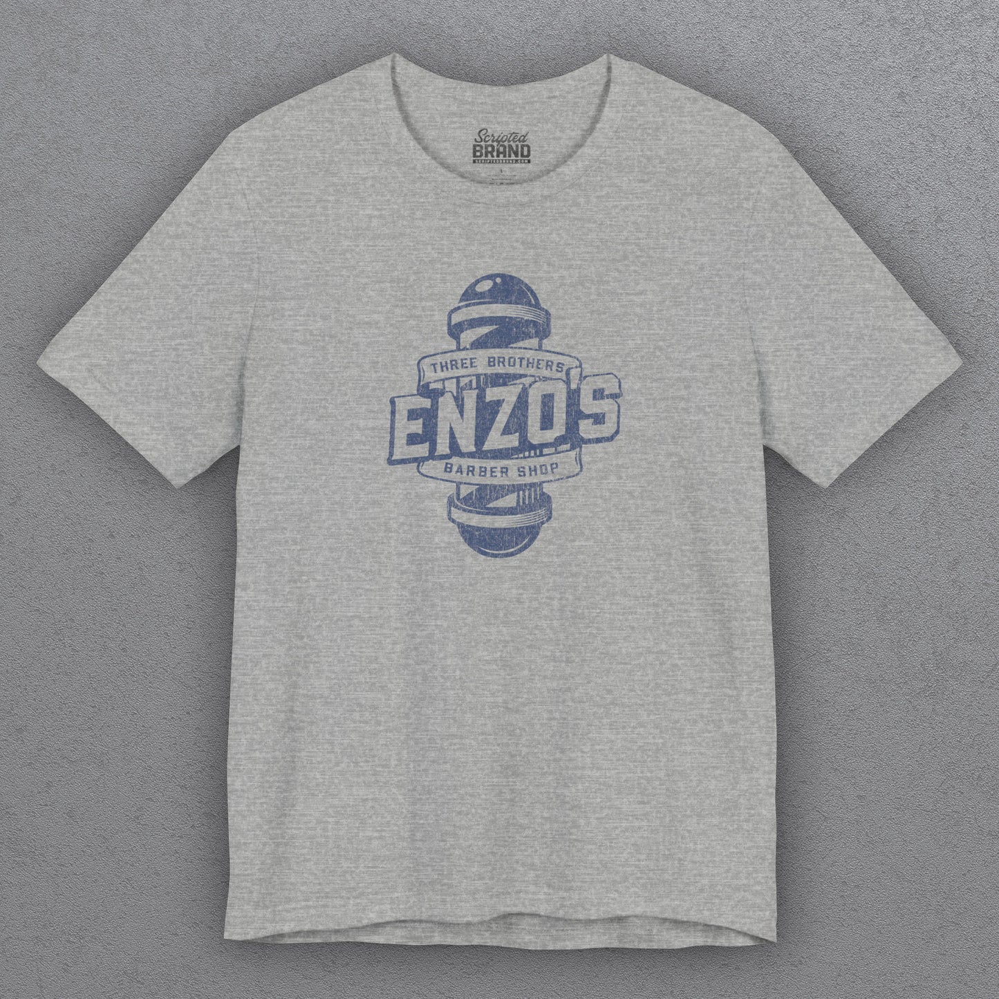 Front view of an athletic heather gray t-shirt with the Enzo's Barber Shop logo graphic inspired by the TV show Seinfeld in a vintage distressed style.