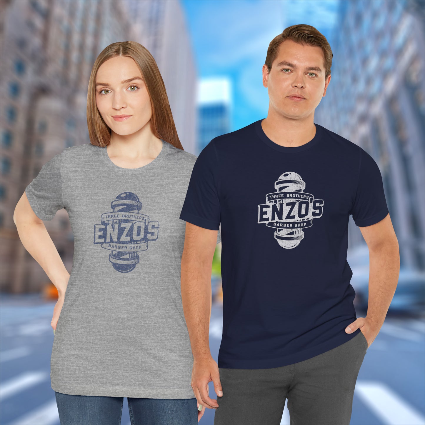 2 models wearing grey and navy soft unisex Bella+Canvas 3001 short-sleeve t-shirts featuring a unique Enzo's Barber Shop logo graphic, designed by ScriptedBrand in a vintage distressed style, and inspired by the TV show Seinfeld.