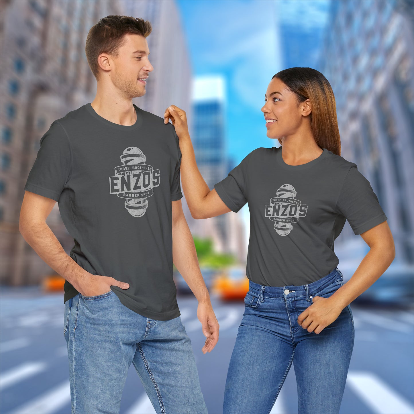 2 models wearing asphalt grey soft unisex Bella+Canvas 3001 short-sleeve t-shirts featuring a unique Enzo's Barber Shop logo graphic, designed by ScriptedBrand in a vintage distressed style, and inspired by the TV show Seinfeld.