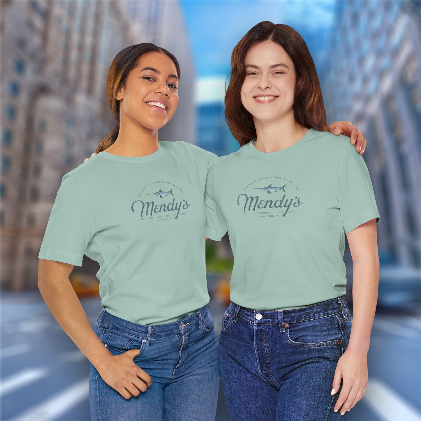 2 female models wearing dusty blue green colored soft unisex Bella+Canvas 3001 short-sleeve t-shirts featuring a unique Mendy's Restaurant logo graphic, designed by ScriptedBrand in a vintage distressed style, and inspired by the TV show Seinfeld.