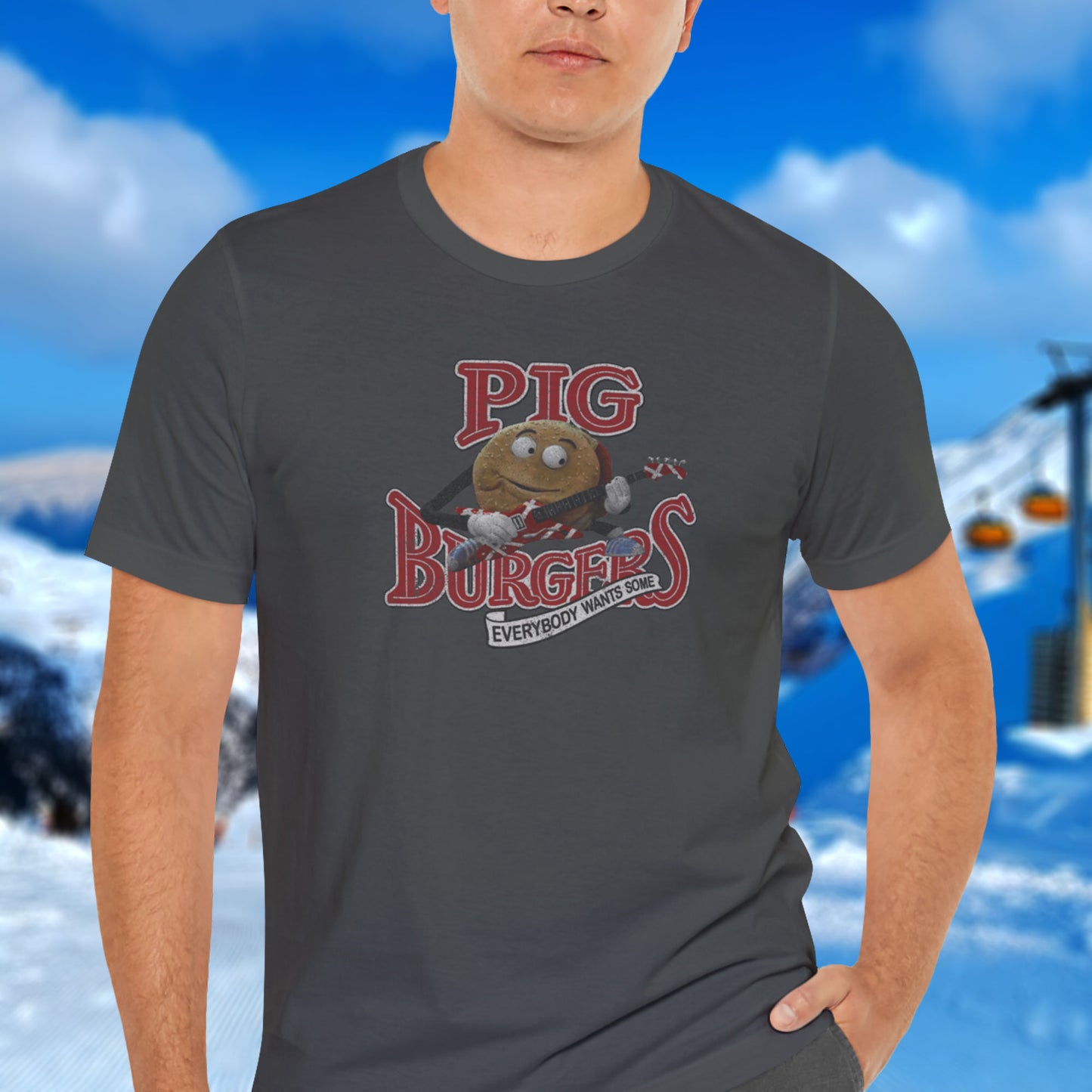 Male model on a ski mountain wearing an athletic heather grey colored soft Bella+Canvas 3001 short-sleeve t-shirt featuring a graphic of the fictional Pig Burgers logo from the movie Better Off Dead, along with the Van Halen singing hamburger playing guitar, with the small subhead phrase EVERYBODY WANTS SOME. The graphic is designed in a vintage distressed style, sold by ScriptedBrand.