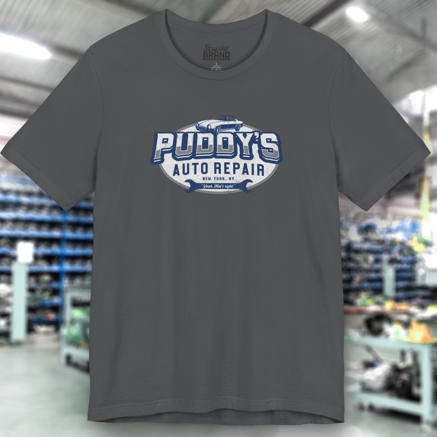 Front view of an asphalt gray soft short-sleeve t-shirt featuring a Puddy's Auto Repair graphic designed by ScriptedBrand inspired by the TV show Seinfeld in a vintage distressed ink-stamped worn-in style.