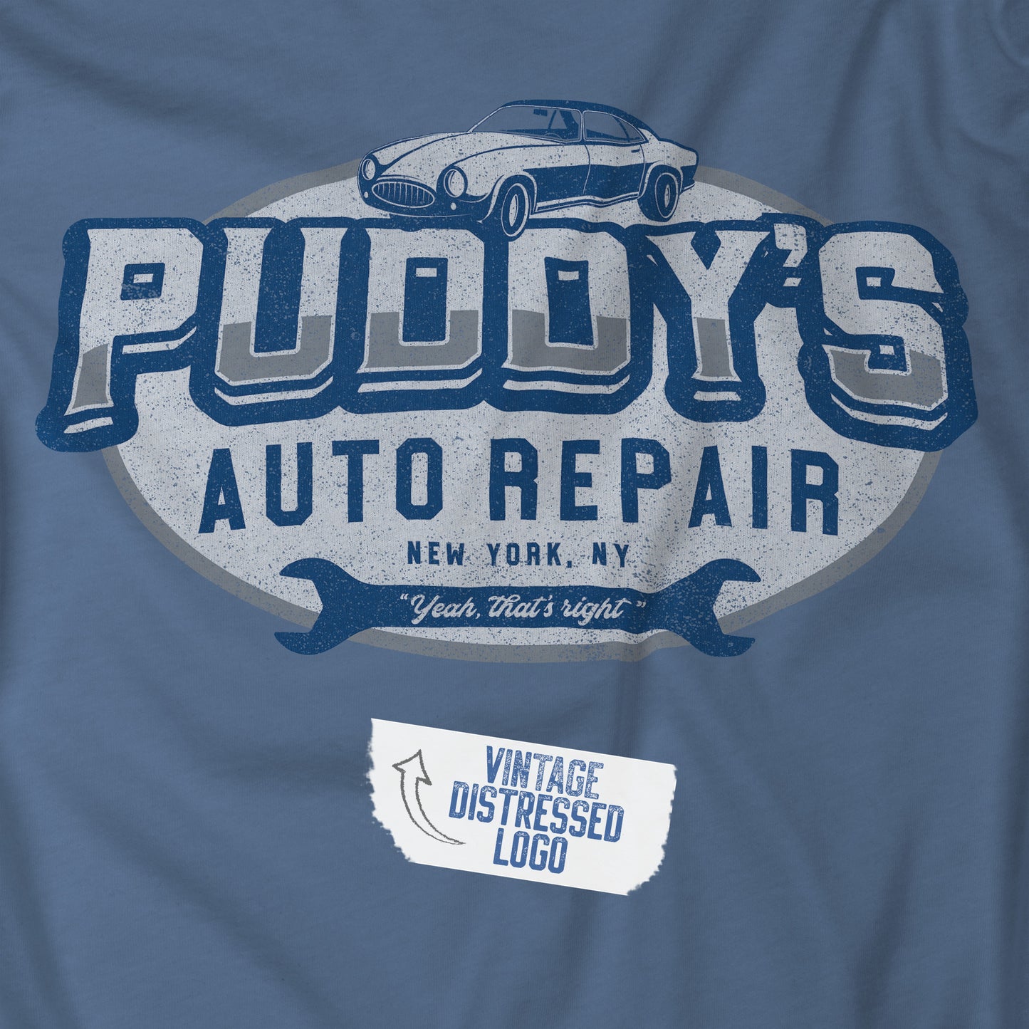 Closeup view of a Lavender Blue Soft short-sleeve t-shirt featuring a Puddy's Auto Repair graphic inspired by the TV show Seinfeld in a vintage distressed ink-stamped worn-in style.