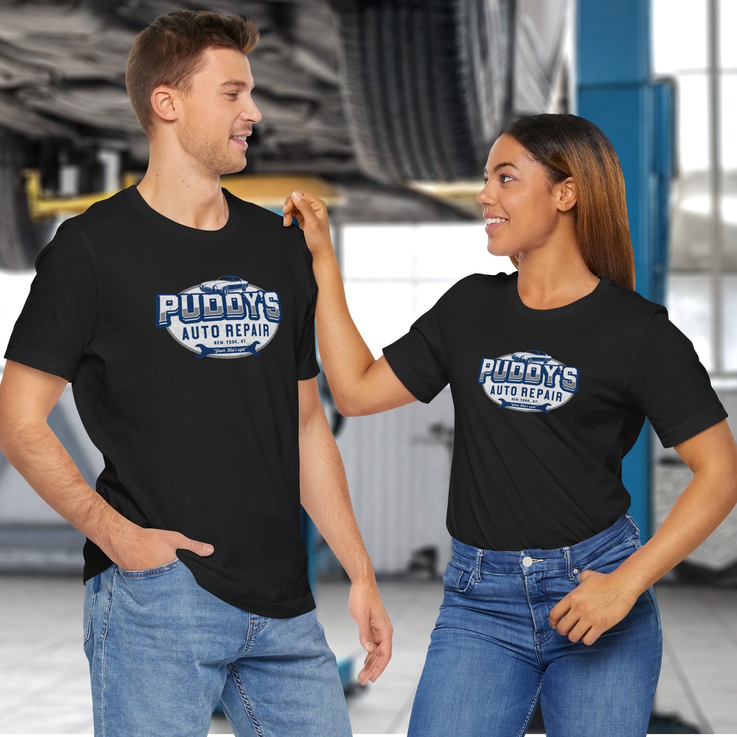 2 models wearing black Soft short-sleeve t-shirts featuring a Puddy's Auto Repair graphic designed by ScriptedBrand inspired by the TV show Seinfeld in a vintage distressed ink-stamped worn-in style.