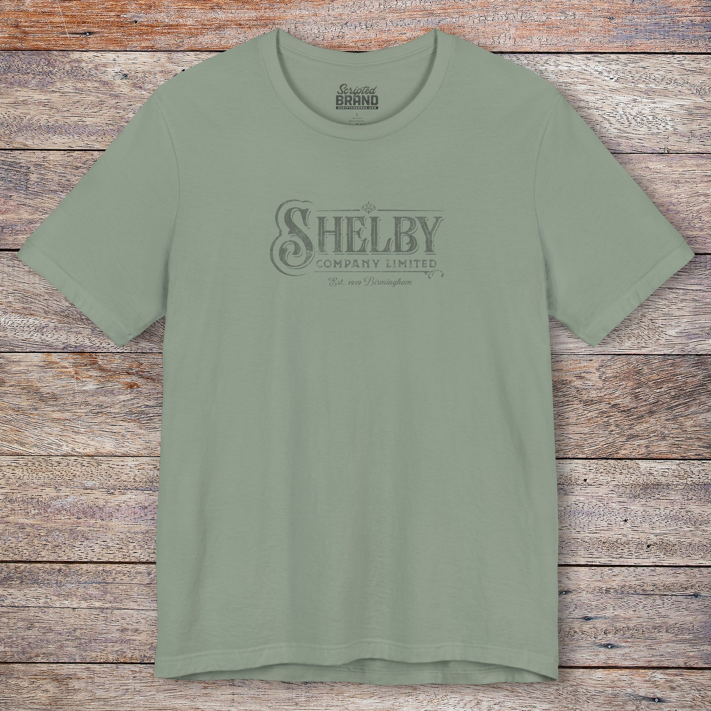 Front view of a sage green soft short-sleeve Bella+Canvas 3001 t-shirt featuring the Shelby Company Limited logo from the show Peaky Blinders in a vintage distressed style, sold by ScriptedBrand.