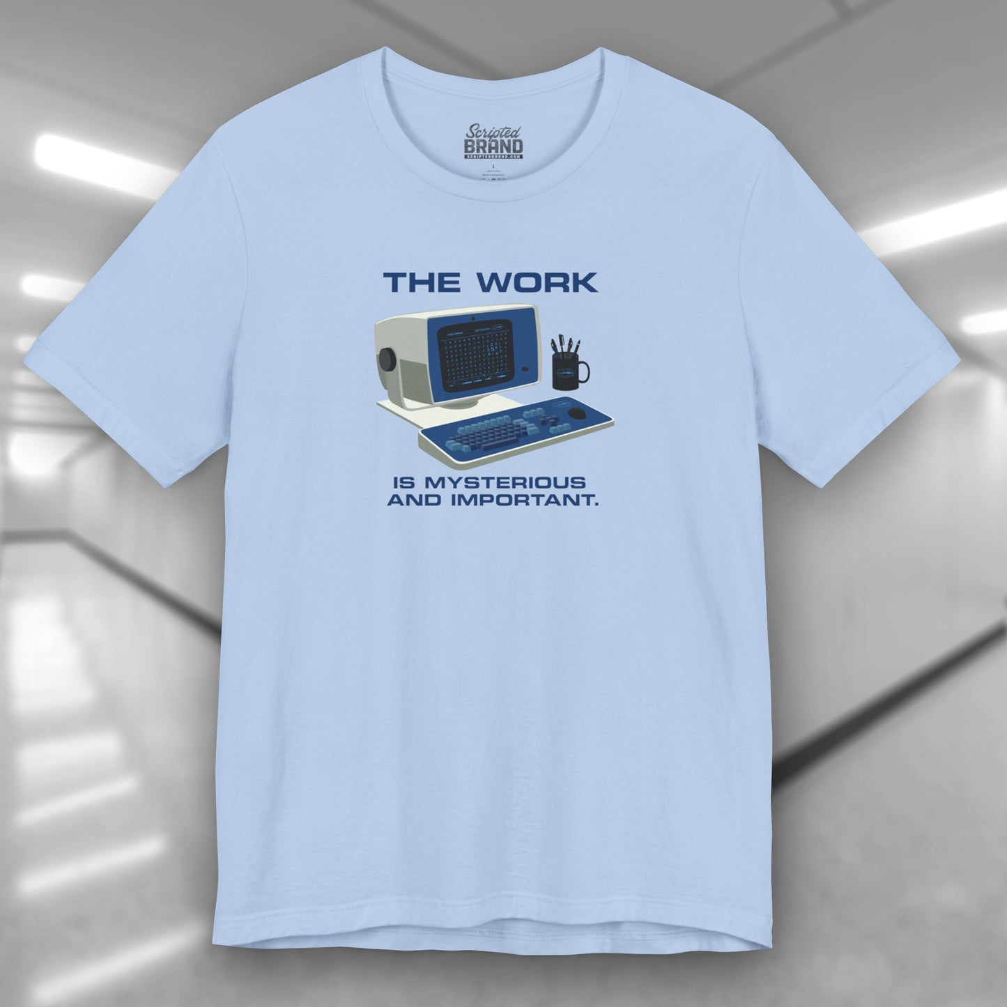 Front view of a baby blue Soft Bella+Canvas shirtsleeve t-shirt featuring the retro computer workstation from the Apple TV show Severance, and includes the text The Work is Mysterious and Important. Graphic is designed and illustrated by ScriptedBrand.