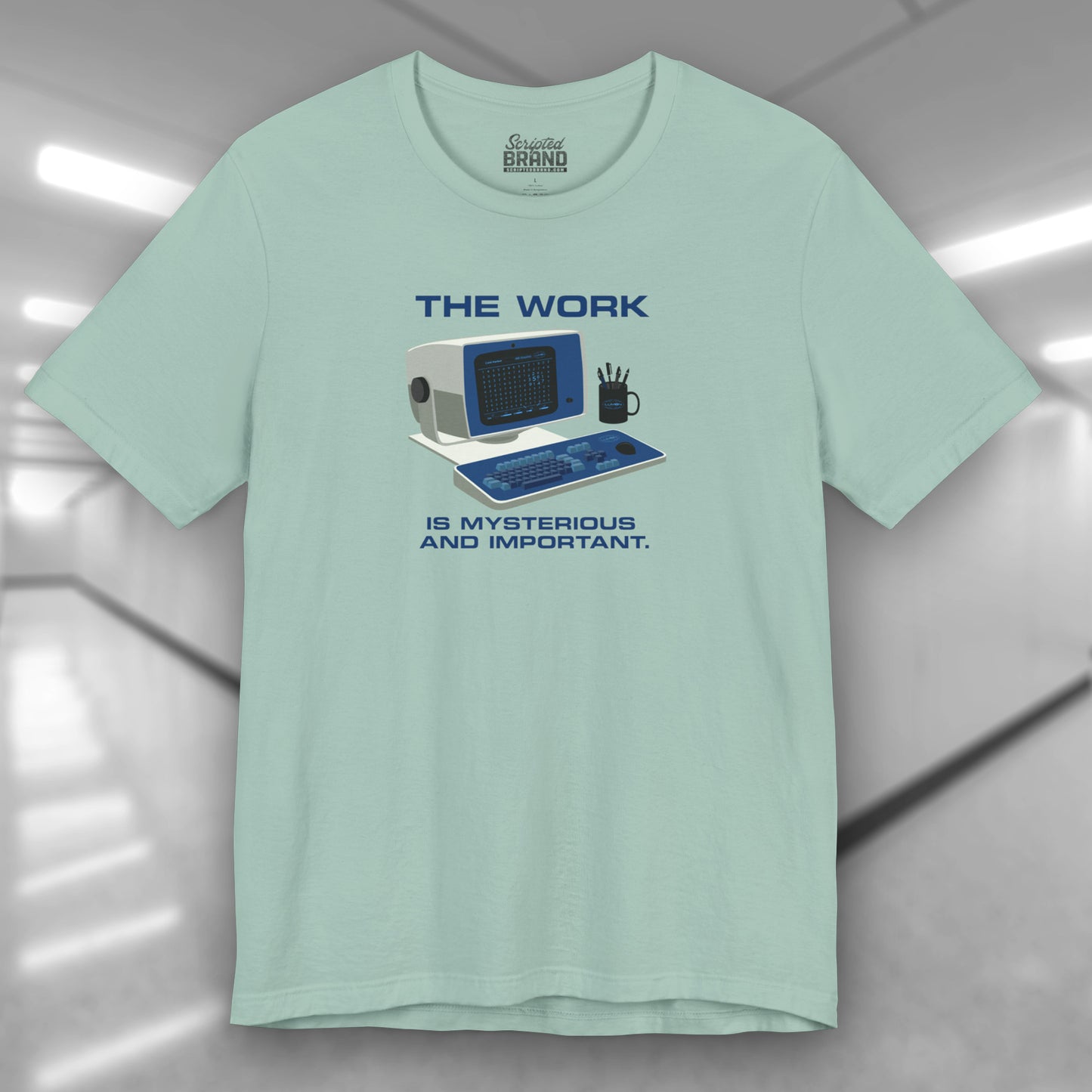 Front view of a dusty blue Soft Bella+Canvas shirtsleeve t-shirt featuring the retro computer workstation from the Apple TV show Severance, and includes the text The Work is Mysterious and Important. Graphic is designed and illustrated by ScriptedBrand.