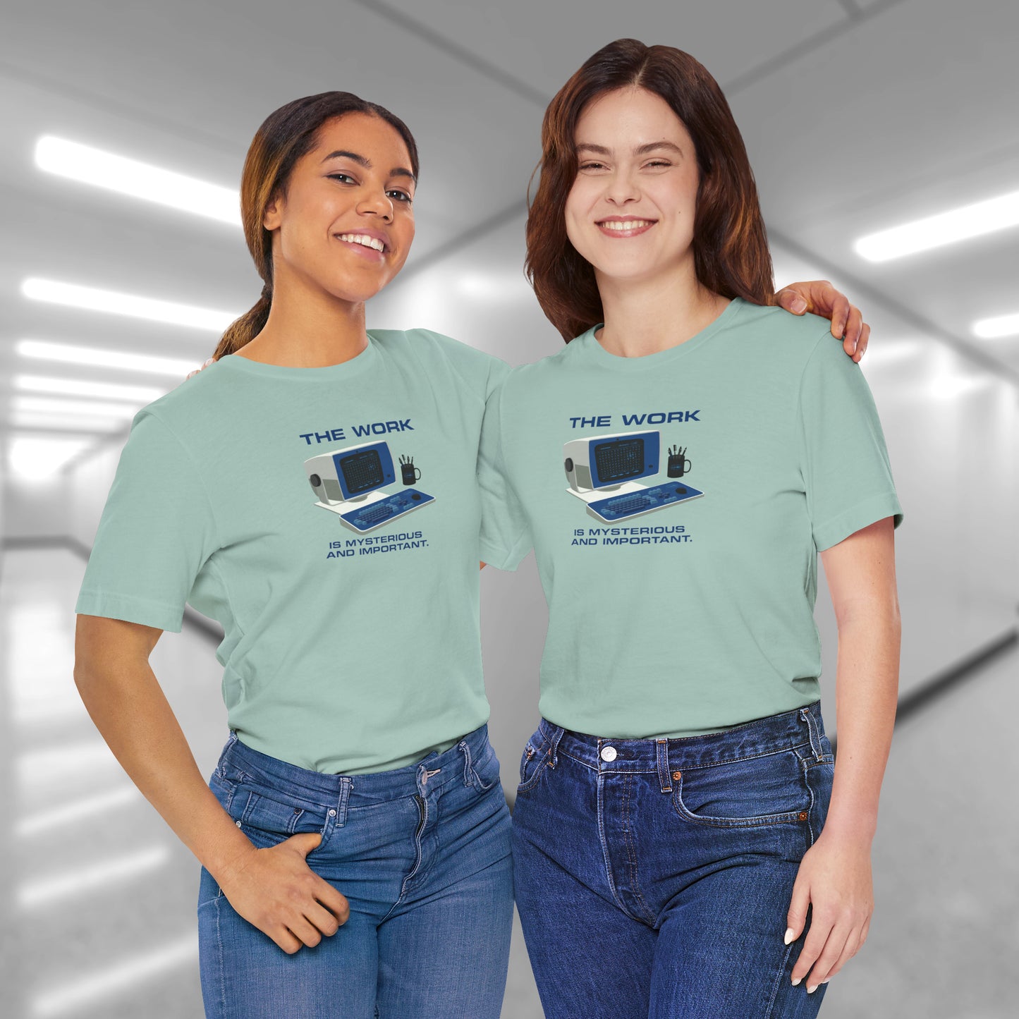 2 Female model wearing dusty blue Soft Bella+Canvas shirtsleeve t-shirts featuring the retro computer workstation from the Apple TV show Severance, and includes the text The Work is Mysterious and Important. Graphic is designed and illustrated by ScriptedBrand.