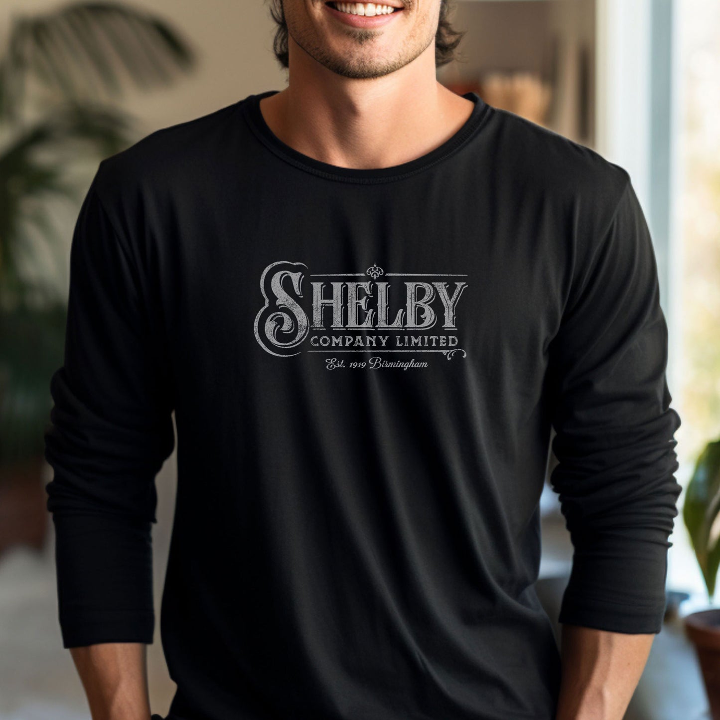 Male model wearing a black soft unisex Bella-Canvas 3501 long-sleeve t-shirt featuring the Shelby Company Limited logo from the show Peaky Blinders in a vintage distressed style, sold by ScriptedBrand.