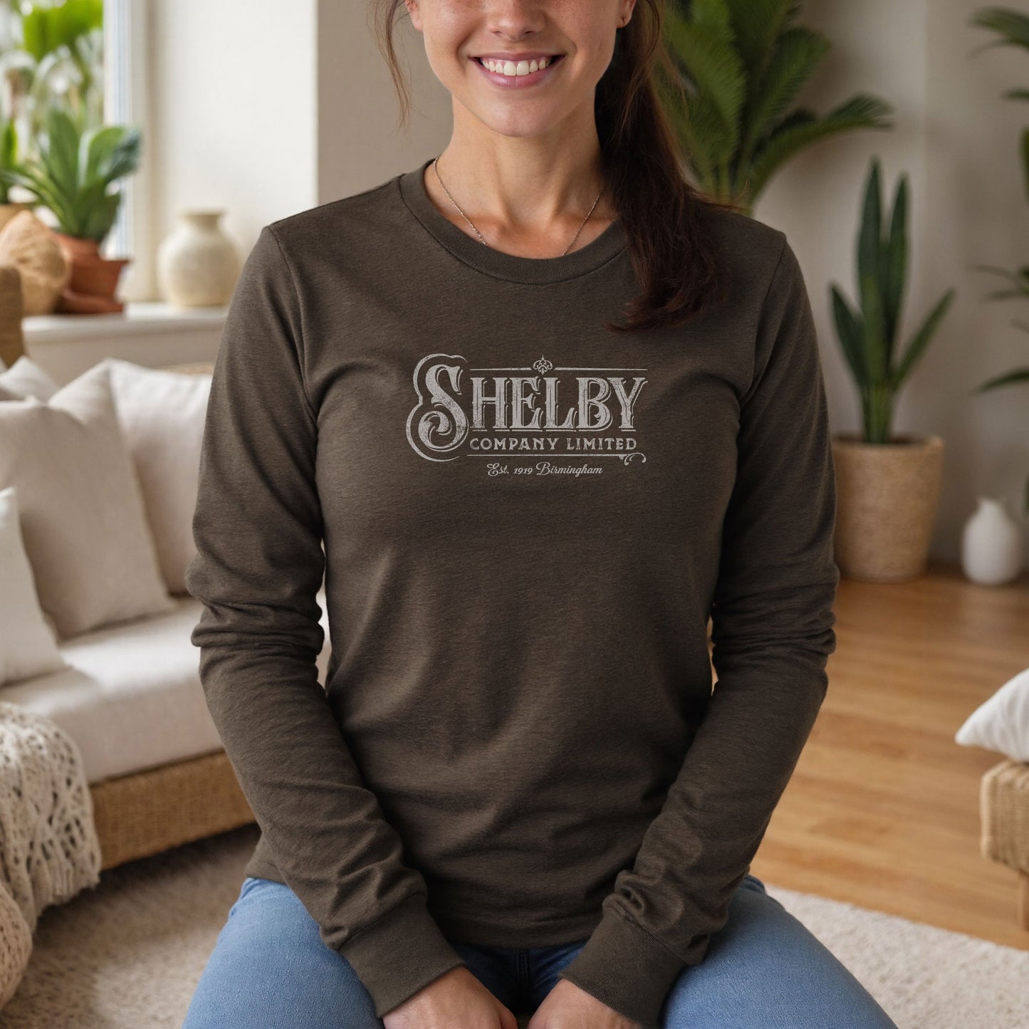 Female model wearing a brown heather soft unisex Bella-Canvas 3501 long-sleeve t-shirt featuring the Shelby Company Limited logo from the show Peaky Blinders in a vintage distressed style, sold by ScriptedBrand.