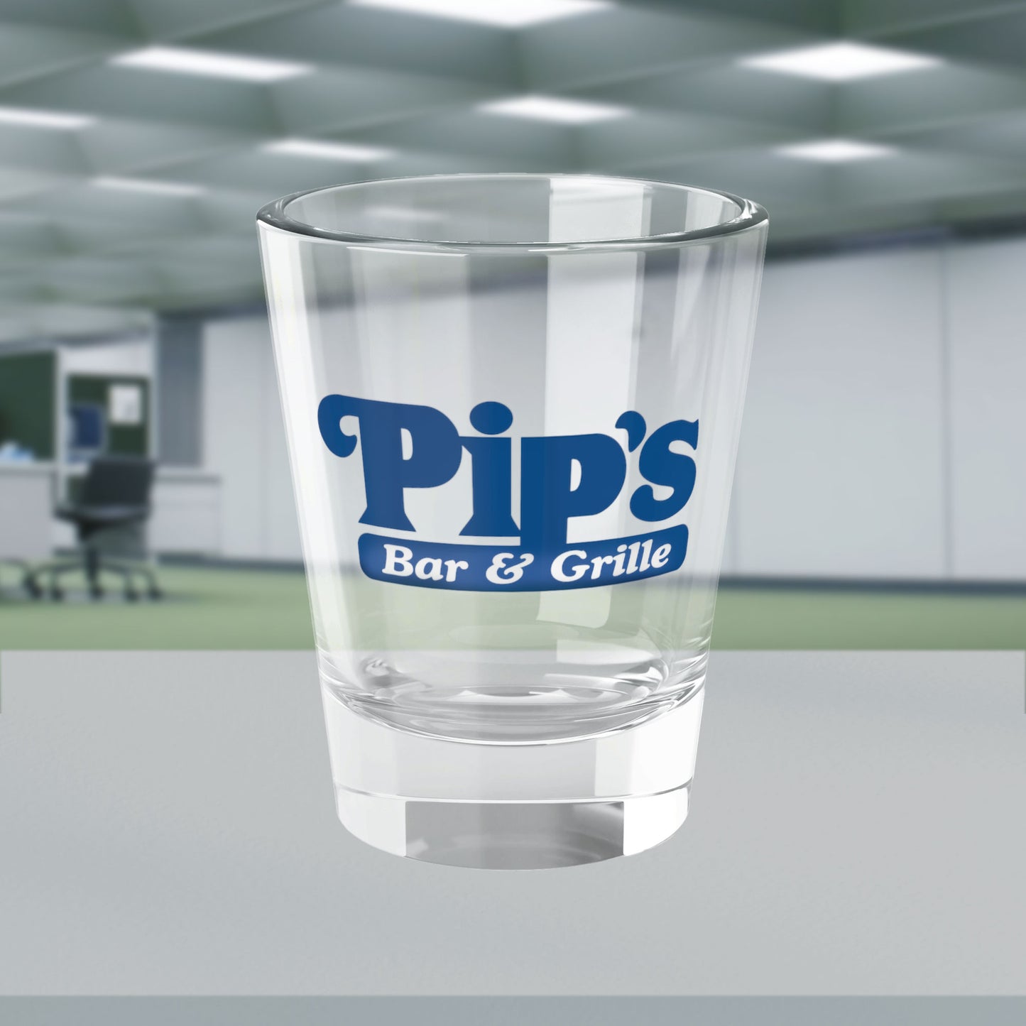 Mockup of a 1.5 oz ounce clear shot glass featuring the Pips Bar and Grill logo from the Apple TV show Severance printed on one side, shown in the Severed Floor of the Lumon Industries building.