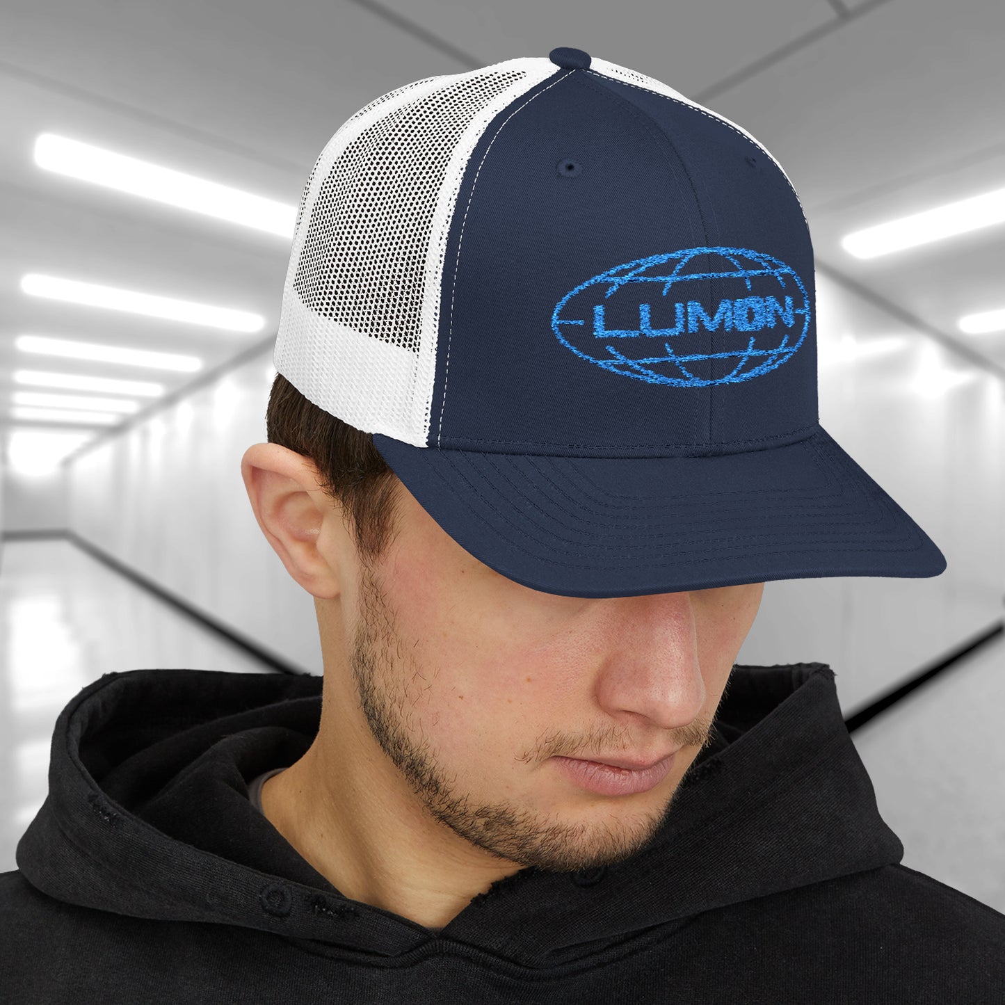 Male model wearing a navy/white Embroidered Snapback Trucker Cap featuring the blue logo of Lumon Industries from the Apple TV Show Severance.