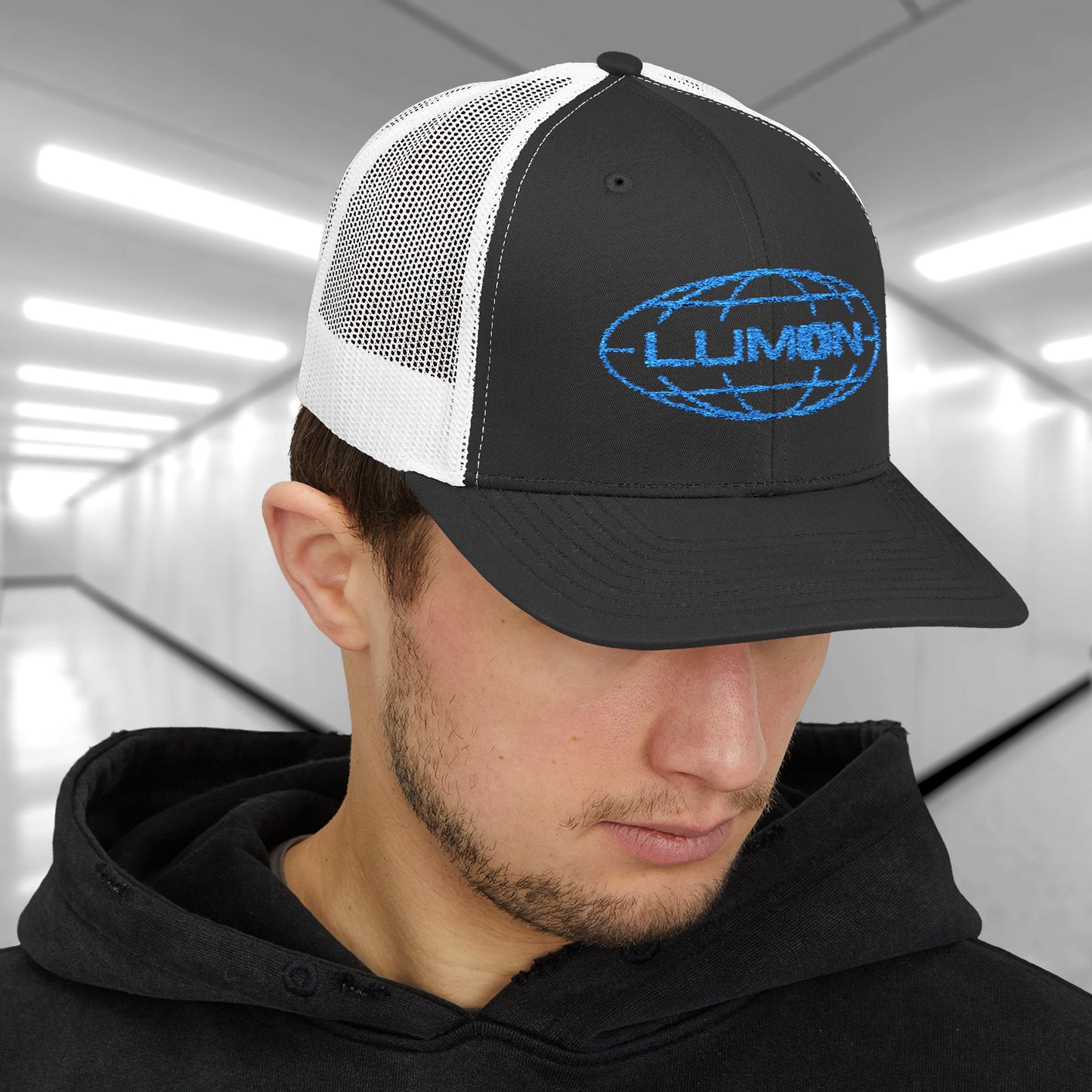 Male model wearing a black/white Embroidered Snapback Trucker Cap featuring the blue logo of Lumon Industries from the Apple TV Show Severance.