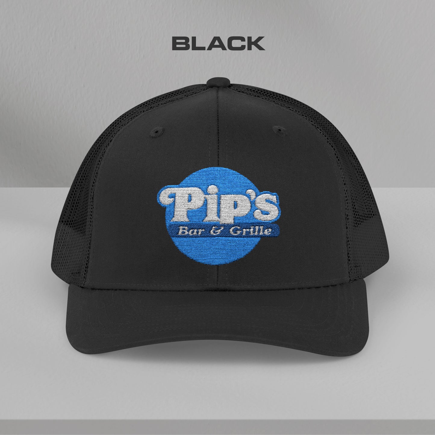 Front view of a black Snapback Trucker Cap featuring an embroidered Pip's Bar and Grill logo from the Apple TV show Severance.