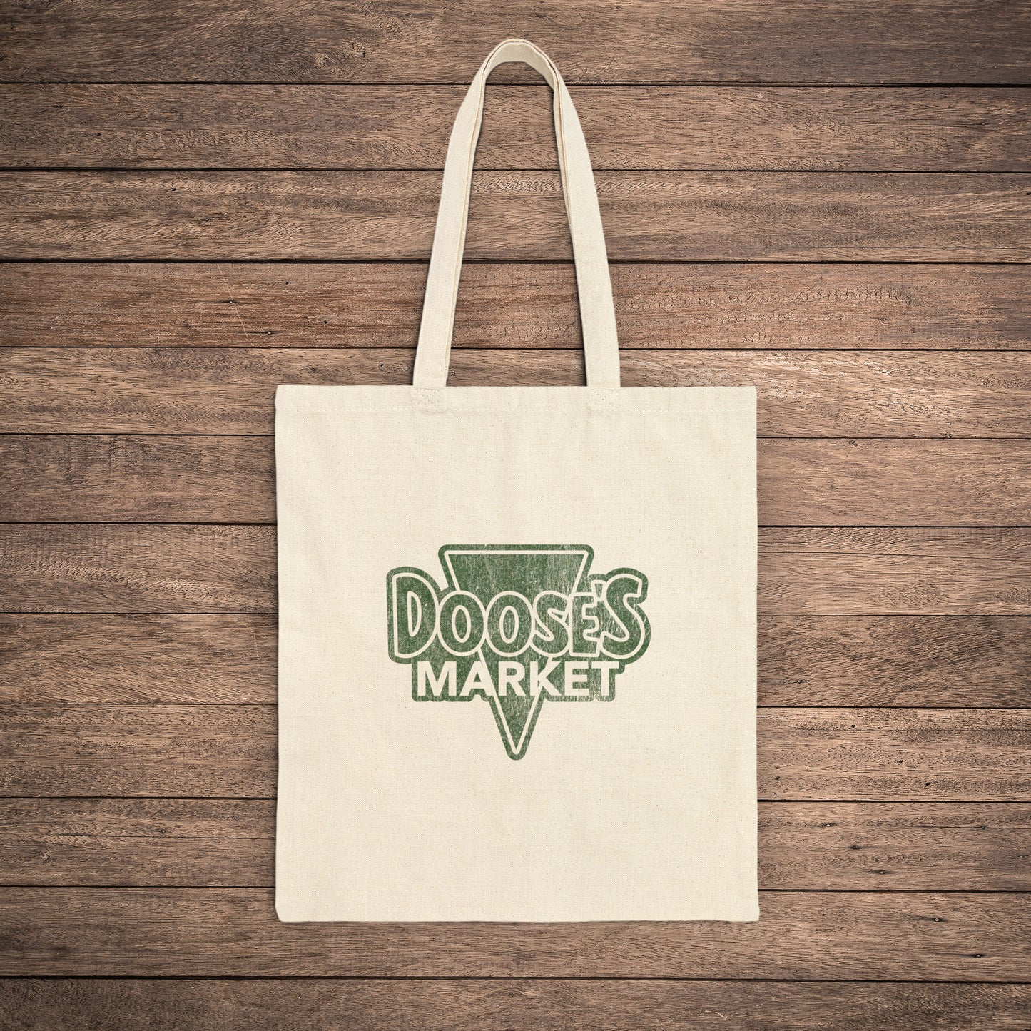 Natural cotton canvas tote bag with vintage green Doose’s Market logo on both sides, inspired by Gilmore Girls, laid flat on wood background.