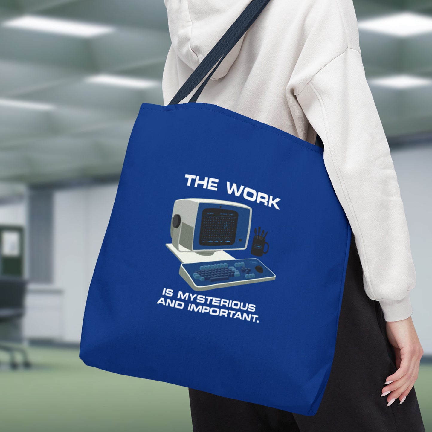 Closeup view of a Female model holding a Large Blue Tote Bag (18" x 18") featuring the retro computer workstation from the Apple TV show Severance, and includes the text The Work is Mysterious and Important. Graphic is designed and illustrated by ScriptedBrand.