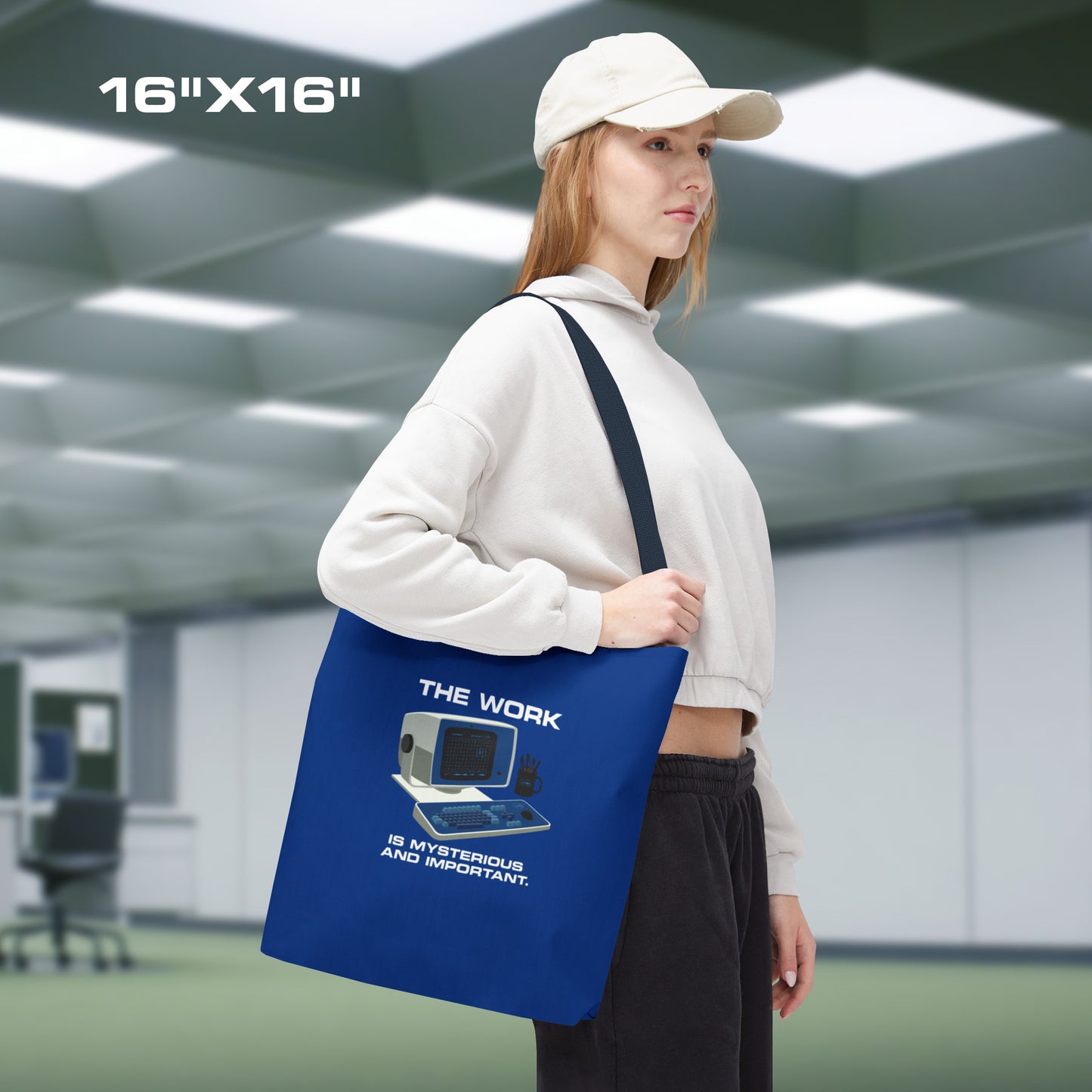 Female model holding a Medium Blue Tote Bag (16" x 16") featuring the retro computer workstation from the Apple TV show Severance, and includes the text The Work is Mysterious and Important. Graphic is designed and illustrated by ScriptedBrand.