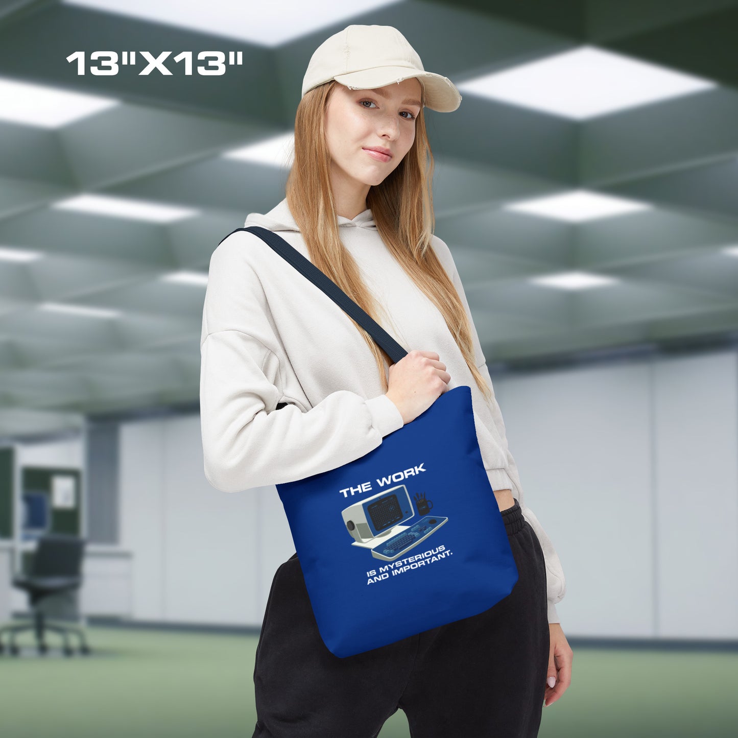 Female model holding a Small Blue Tote Bag (13" x 13") featuring the retro computer workstation from the Apple TV show Severance, and includes the text The Work is Mysterious and Important. Graphic is designed and illustrated by ScriptedBrand.