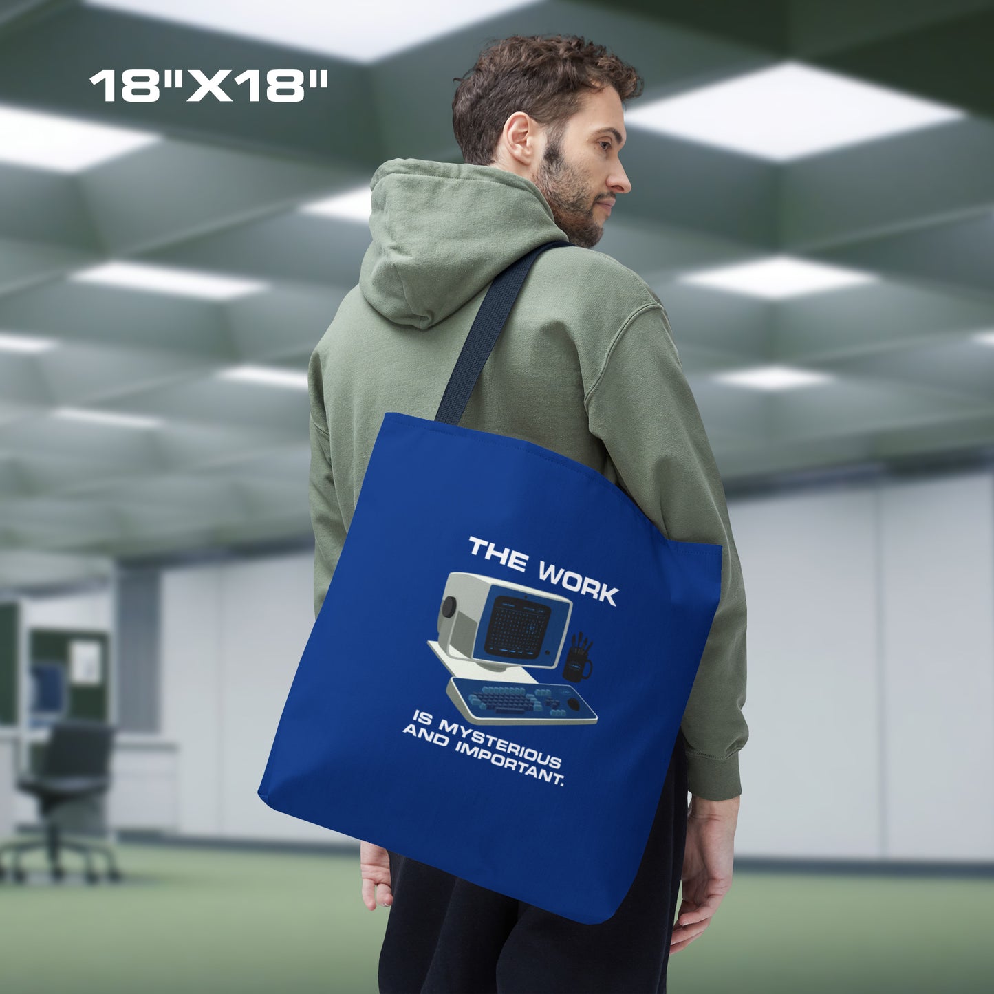 Male model holding a Large Blue Tote Bag (18" x 18") featuring the retro computer workstation from the Apple TV show Severance, and includes the text The Work is Mysterious and Important. Graphic is designed and illustrated by ScriptedBrand.