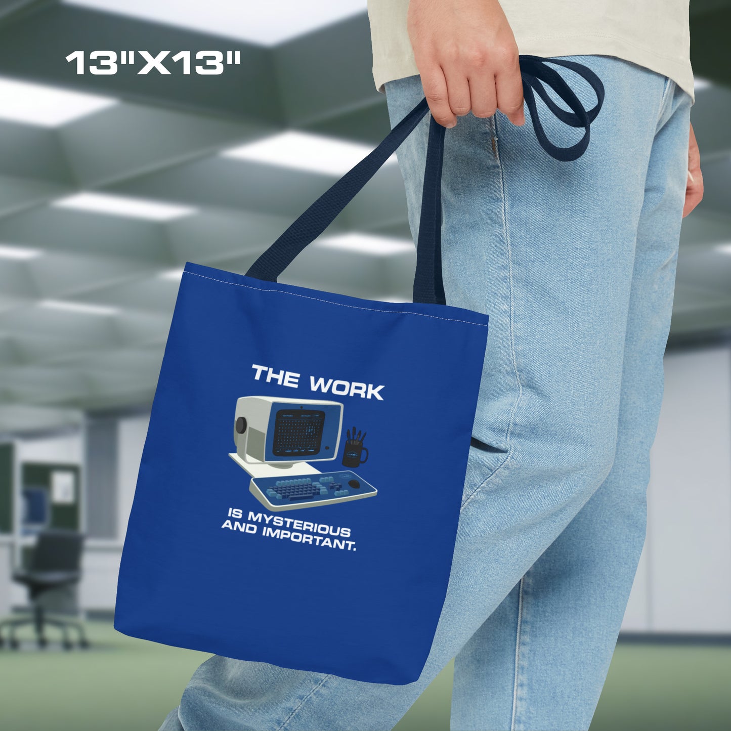 Male model holding a Small Blue Tote Bag (13" x 13") featuring the retro computer workstation from the Apple TV show Severance, and includes the text The Work is Mysterious and Important. Graphic is designed and illustrated by ScriptedBrand.