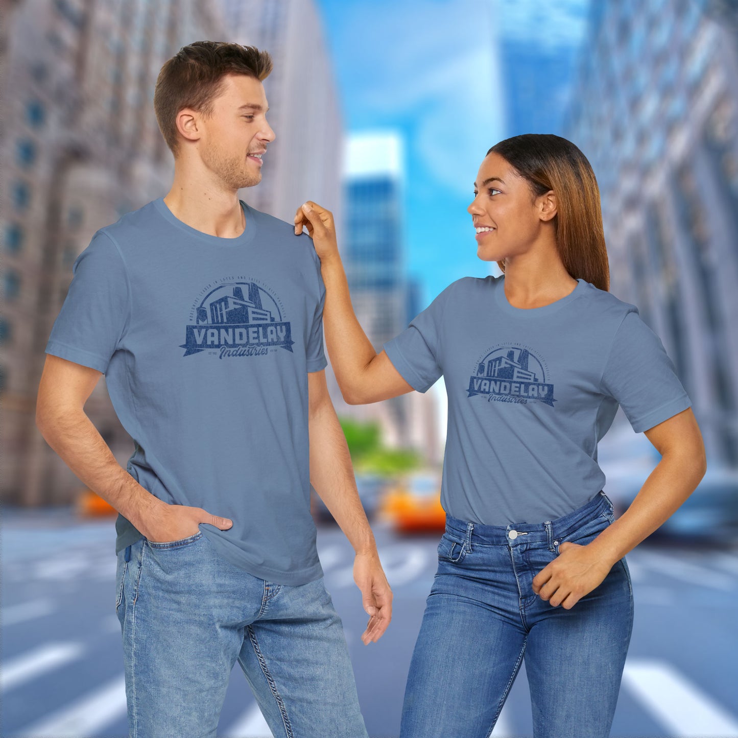 2 models wearing steel blue Soft Bella+Canvas 3001 short-sleeve t-shirts featuring a Vandelay Industries logo graphic, uniquely designed by ScriptedBrand in a vintage distressed style. The fictional company is part of the George Costanza storyline in the TV show Seinfeld.