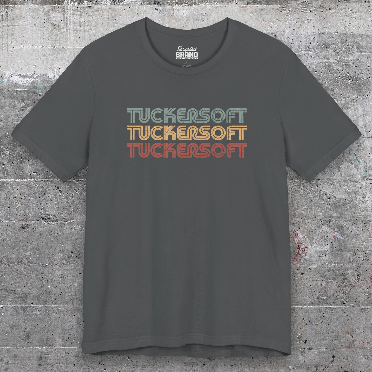 Front view of an asphalt grey colored soft Bella+Canvas 3001 short-sleeve t-shirt tee featuring a logo graphic of the 1980s fictional video game company Tuckersoft inspired by the TV show Black Mirror and the episode Bandersnatch in a vintage distressed style, sold by ScriptedBrand.