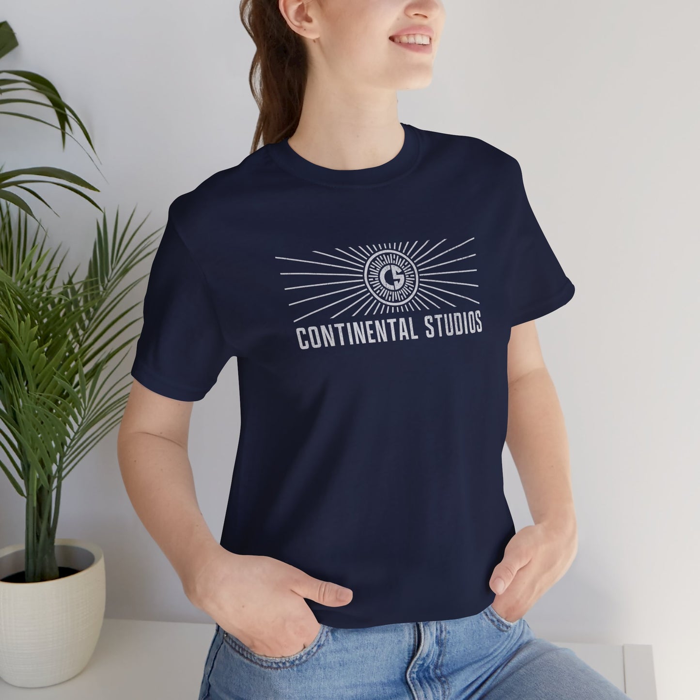 Female model wearing a navy colored Soft Bella+Canvas 3001 short-sleeve t-shirt featuring the logo graphic of the fictional movie studio Continental Studios inspired by the Apple TV show The Studio in a vintage distressed style, sold by ScriptedBrand.